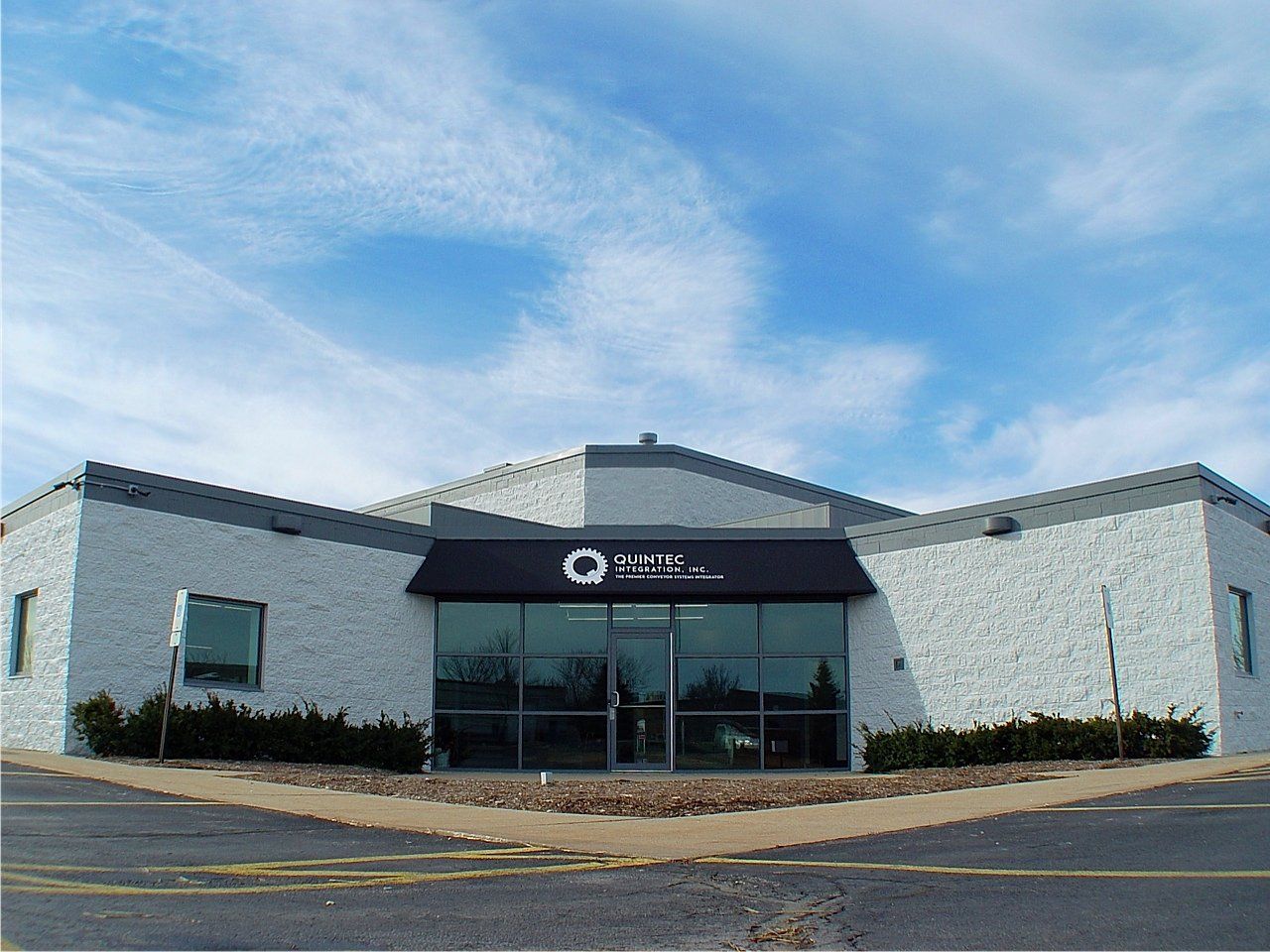 Gray building with black awning over glass doors; blue sky.