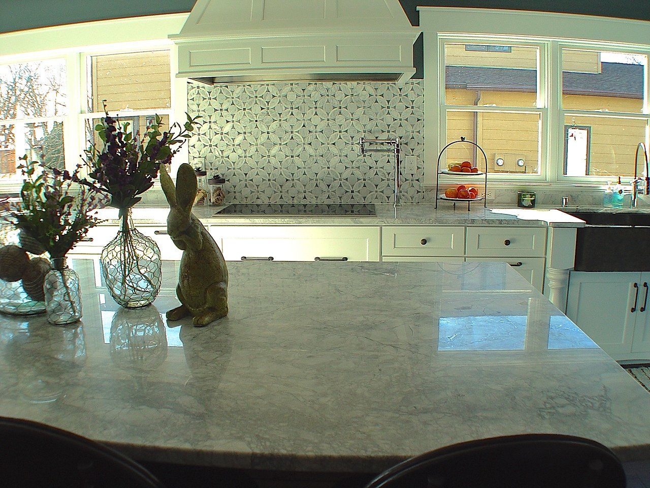 Kitchen island with marble countertop, decorations, and a stove in the background. Windows provide natural light.