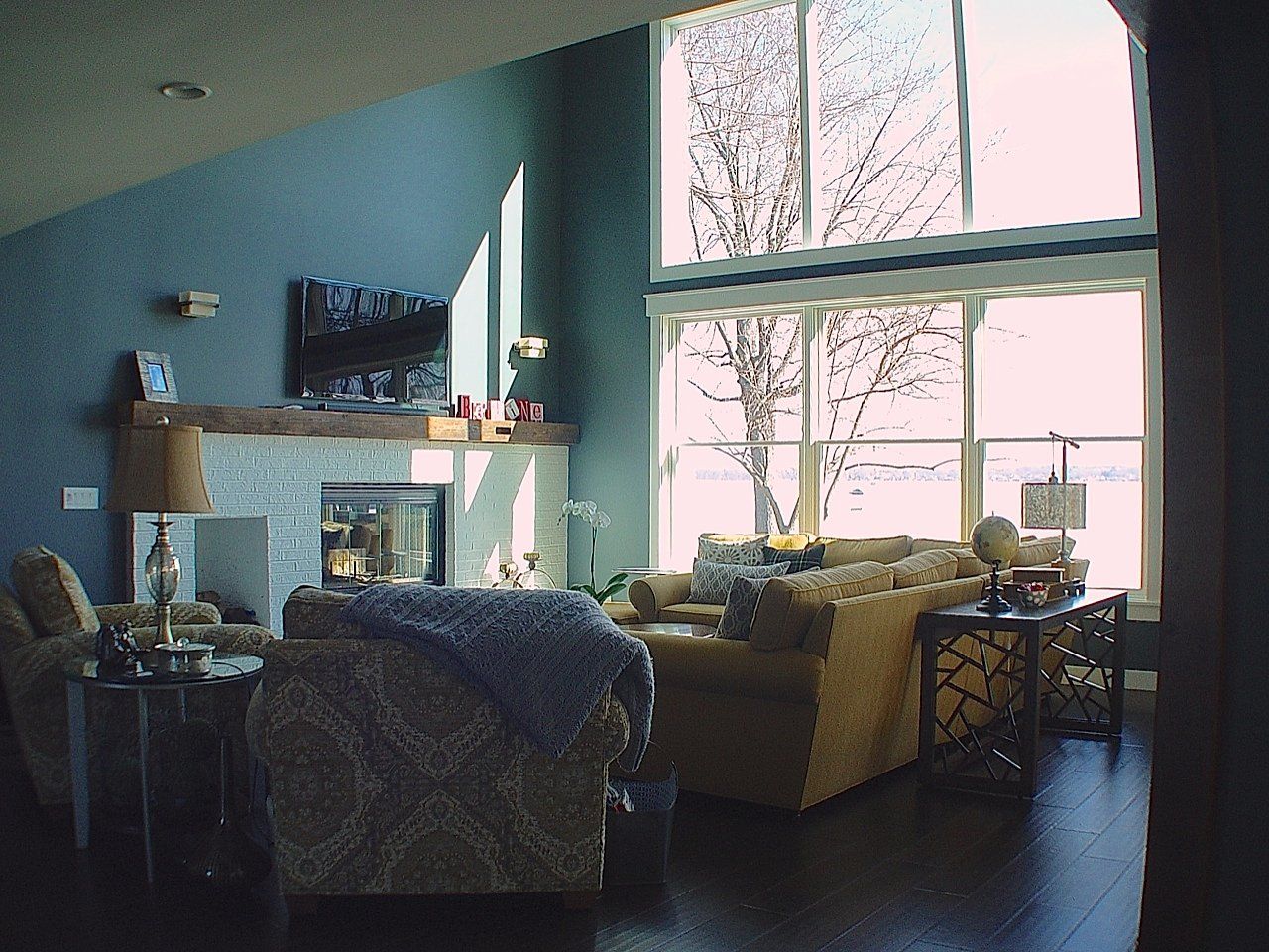 Living room with large windows overlooking a snowy landscape; fireplace, seating, and decorative items.