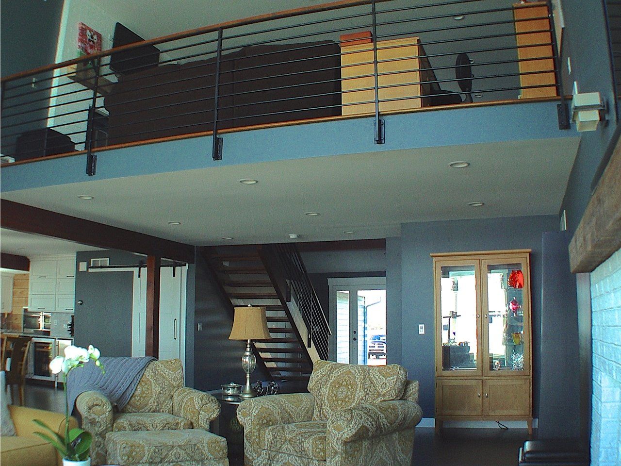 Interior view of a modern loft space with a mezzanine, wooden staircase, and seating area.