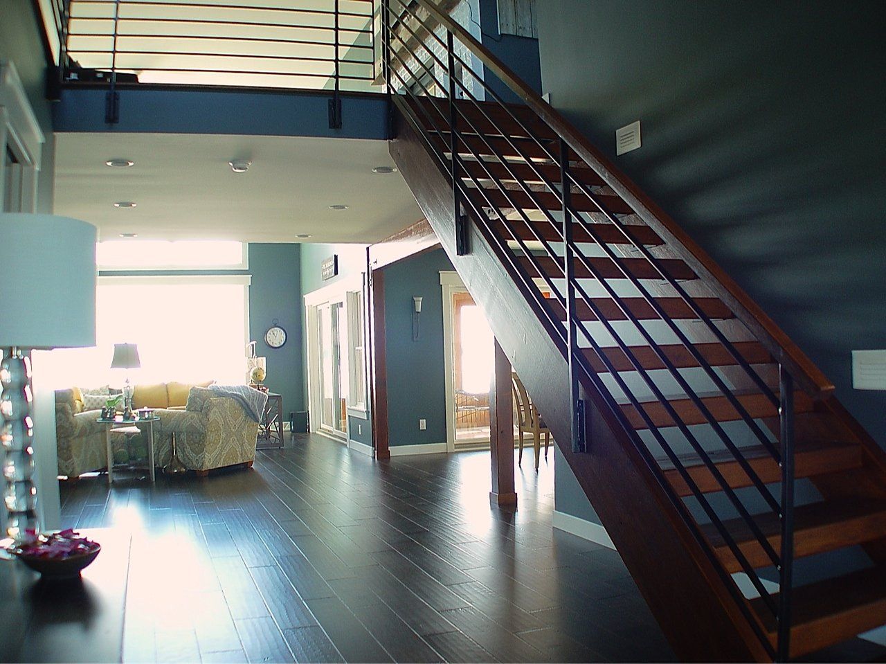 Wooden staircase with metal railing in modern home, dark wood floor, blue-gray walls, open layout.