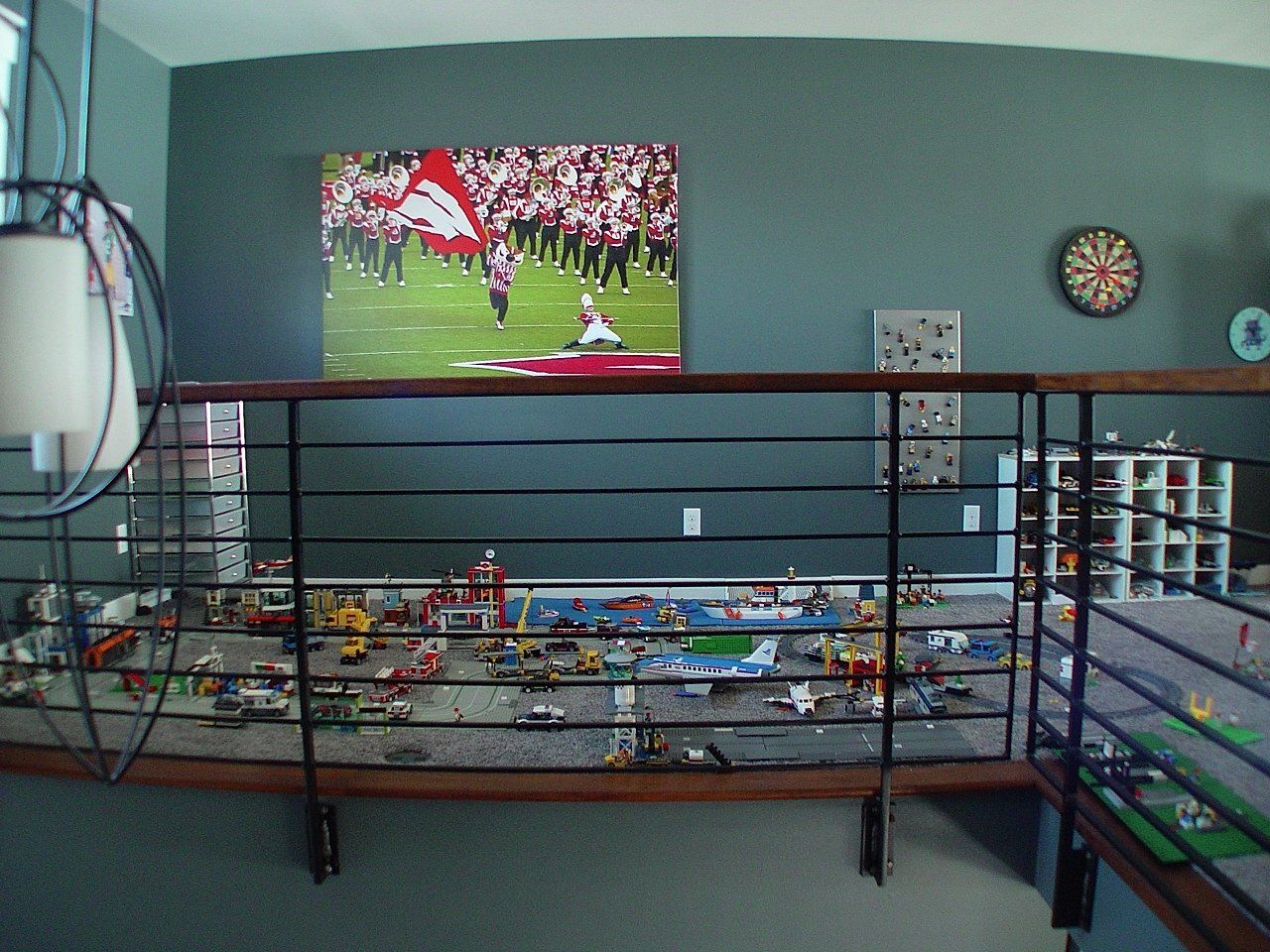 Lego city diorama on shelf, with metal railing, against a teal wall. Sports photo above.
