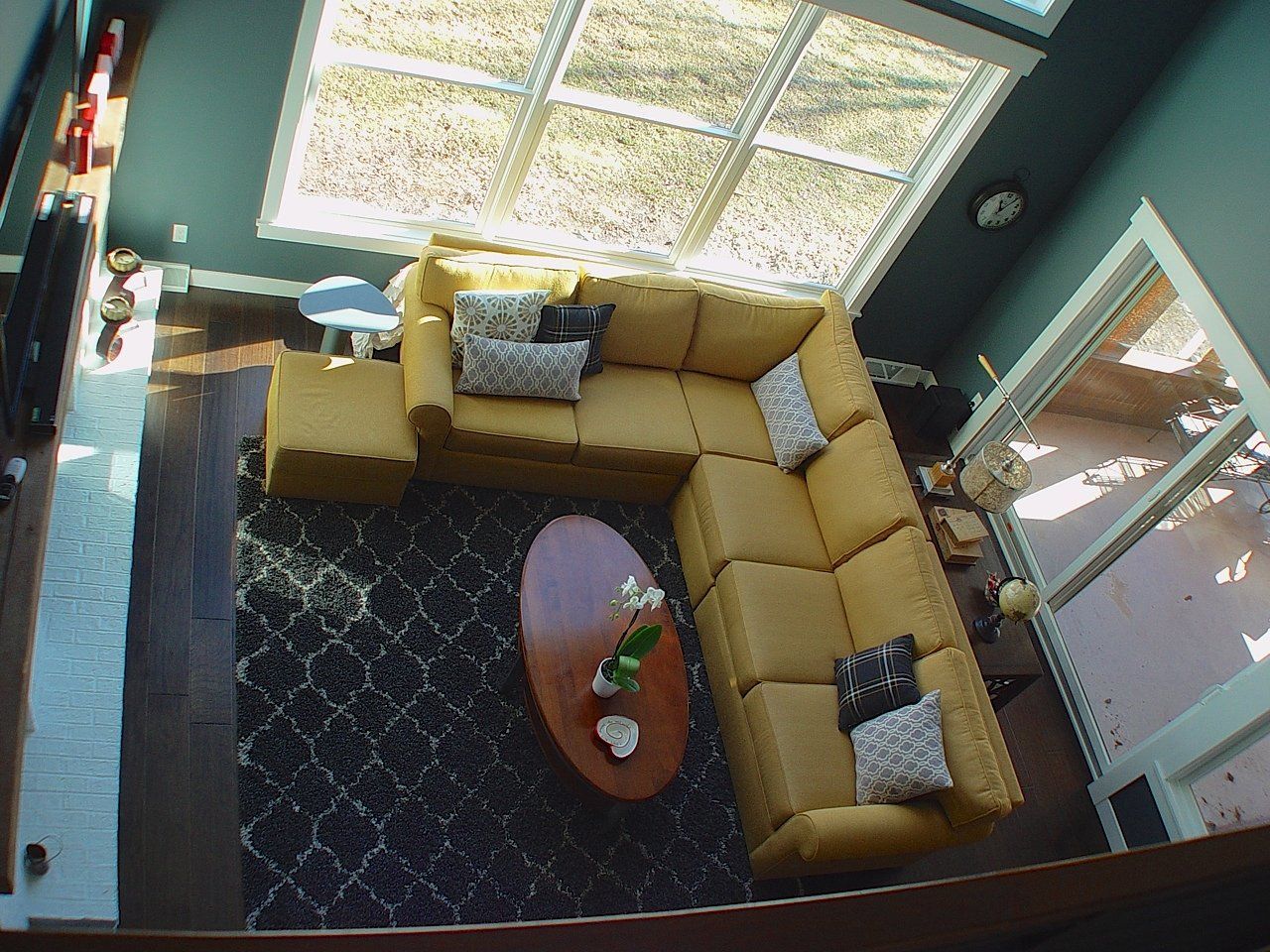 Overhead view of a living room with a yellow sectional sofa, rug, and round coffee table under a skylight.