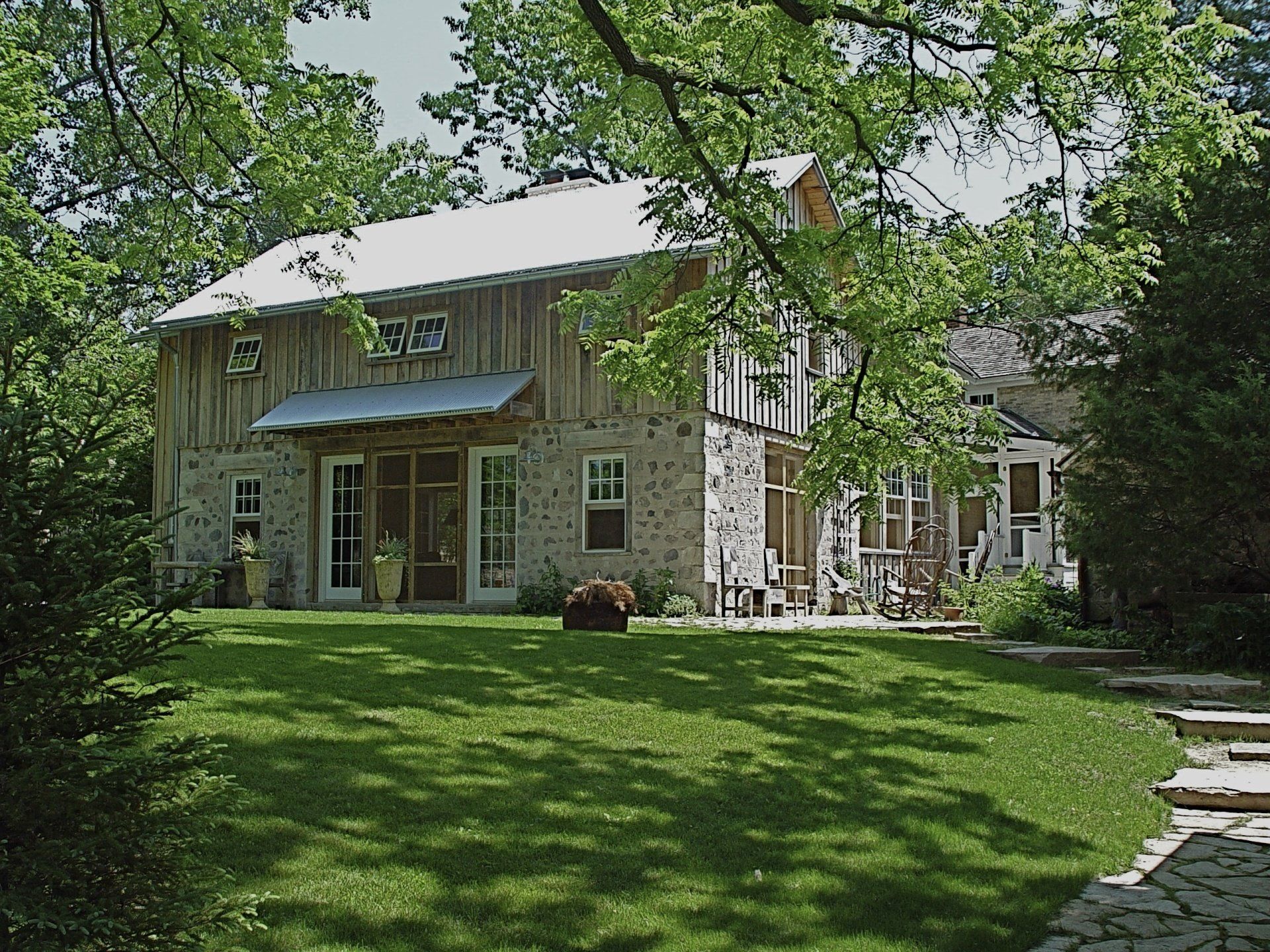 Stone and wood building with porch and metal roof, surrounded by green grass and trees.