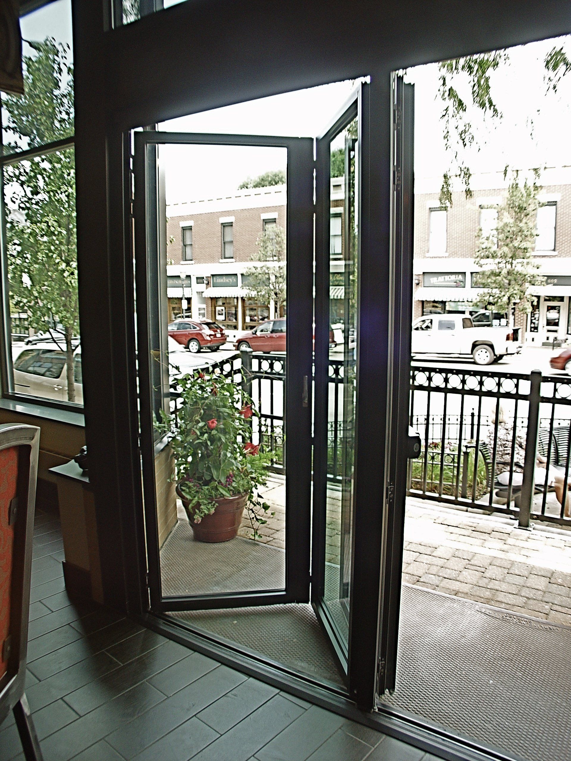 Folding glass doors open to a patio; brick floor, potted plant, street view.