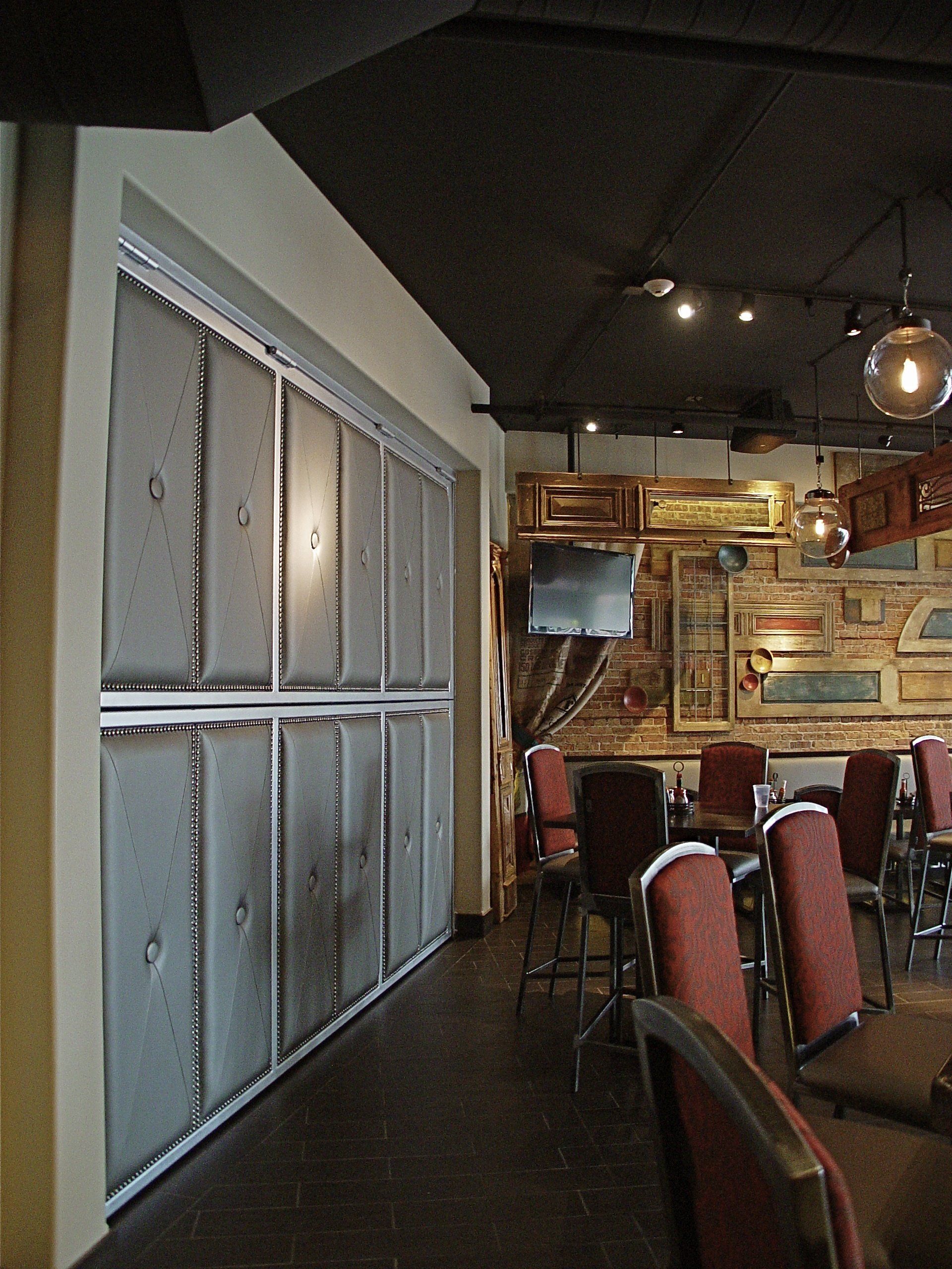 Interior of a bar with a sliding metal door and tables with chairs. The walls are decorated with old windows and a TV.