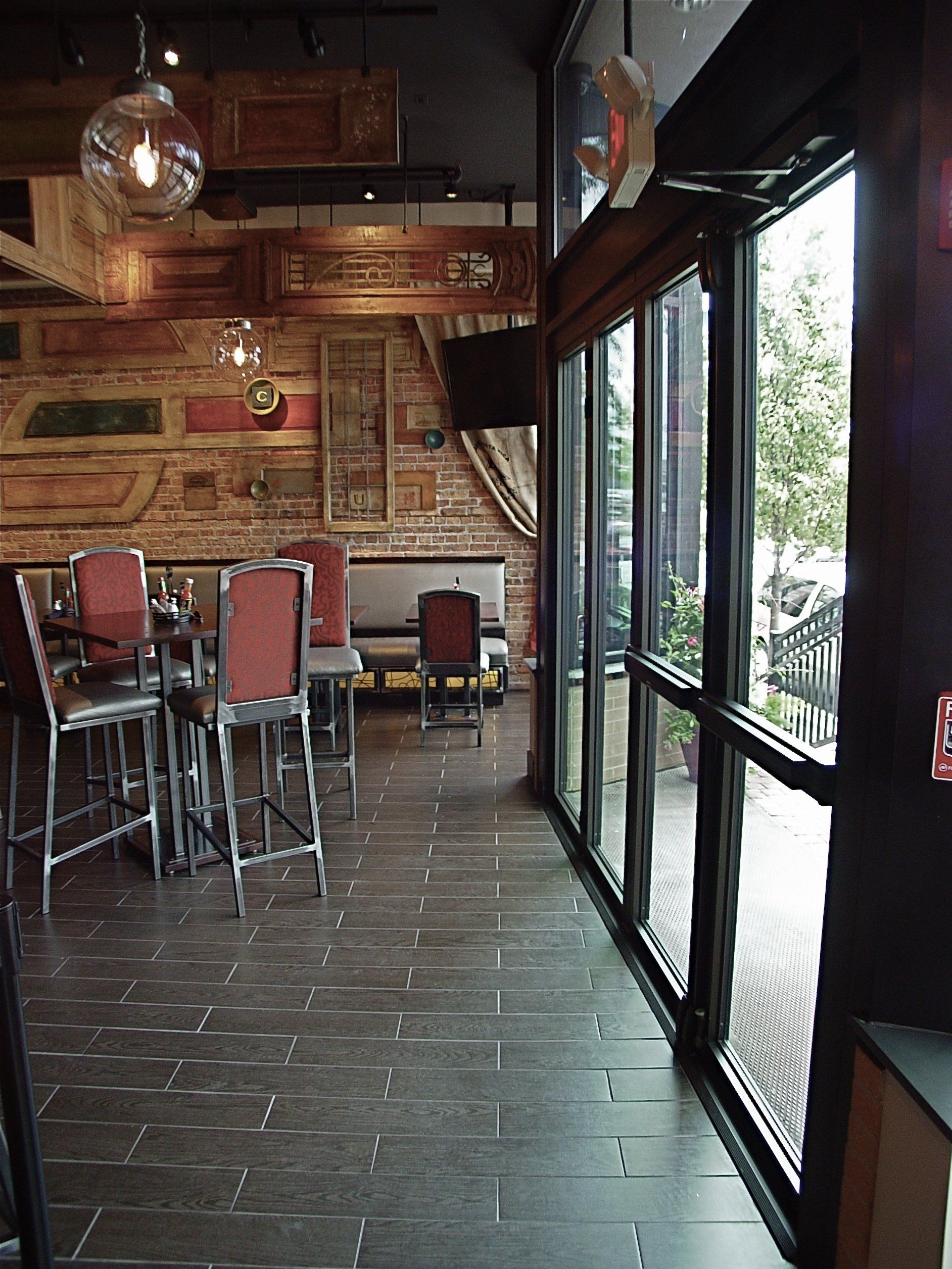 Interior of a restaurant with brick wall decor, tall bar stools, and a large glass door leading outside.