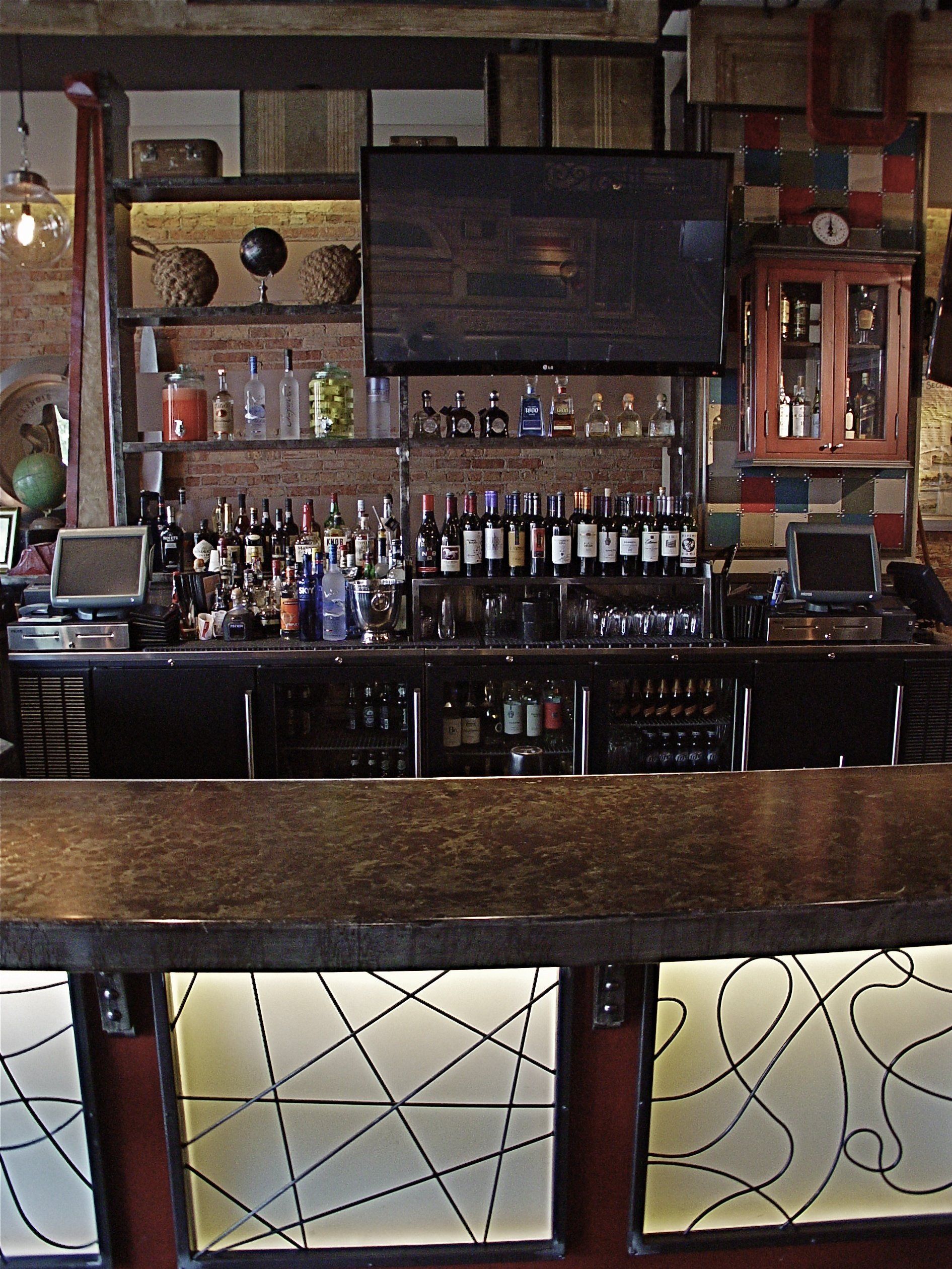 Bar with bottles, glasses, TV screen, and illuminated panels.