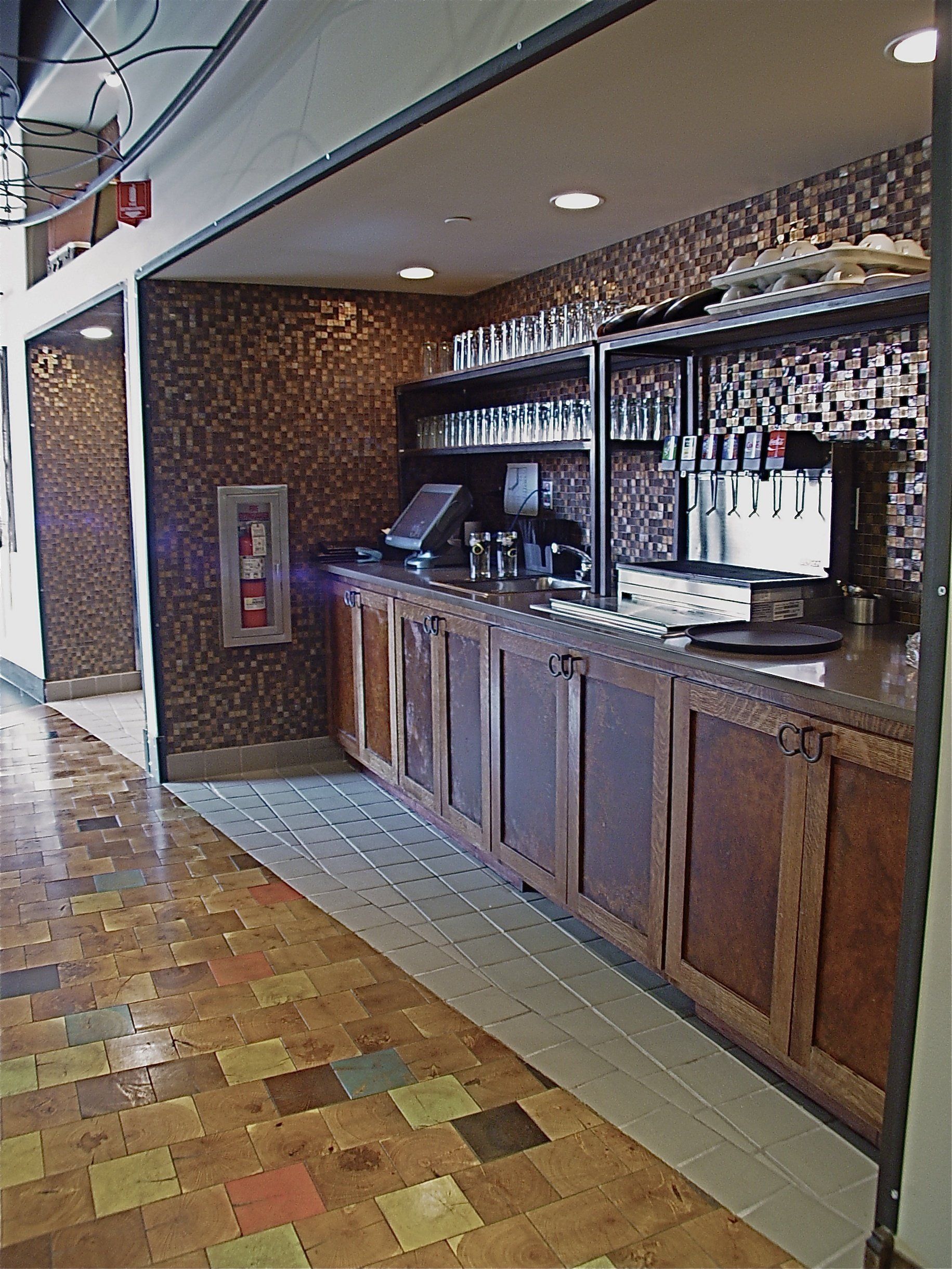 Bar with brown wooden cabinets, tiled backsplash, and tap system.  Striped flooring.