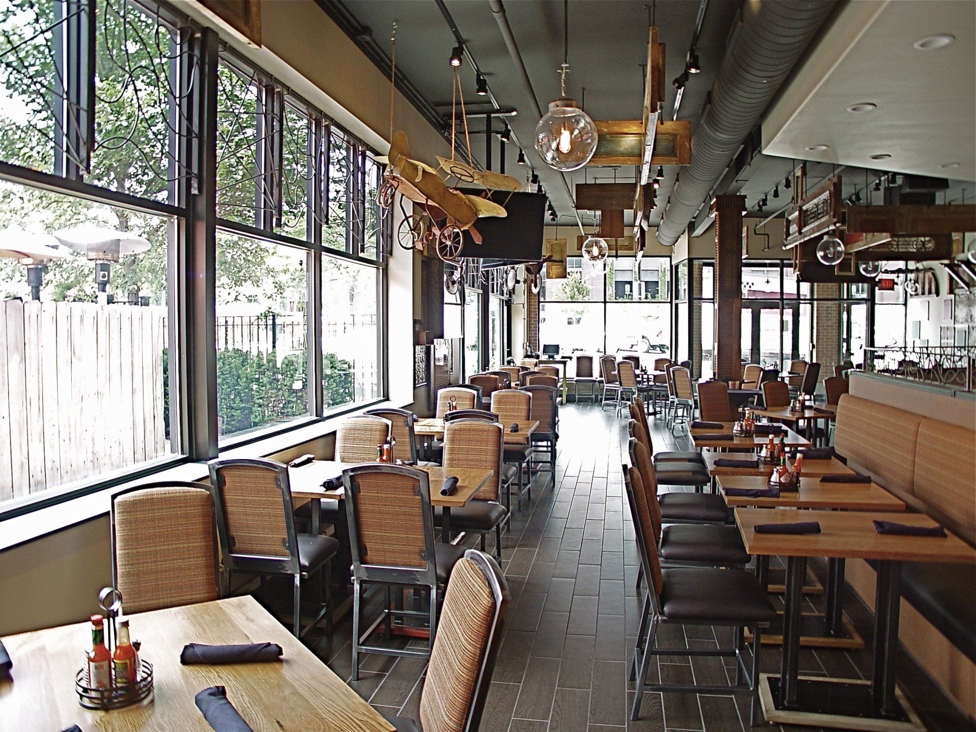 Restaurant interior with tables and chairs near large windows; decorative ceiling lights and wooden airplane models.