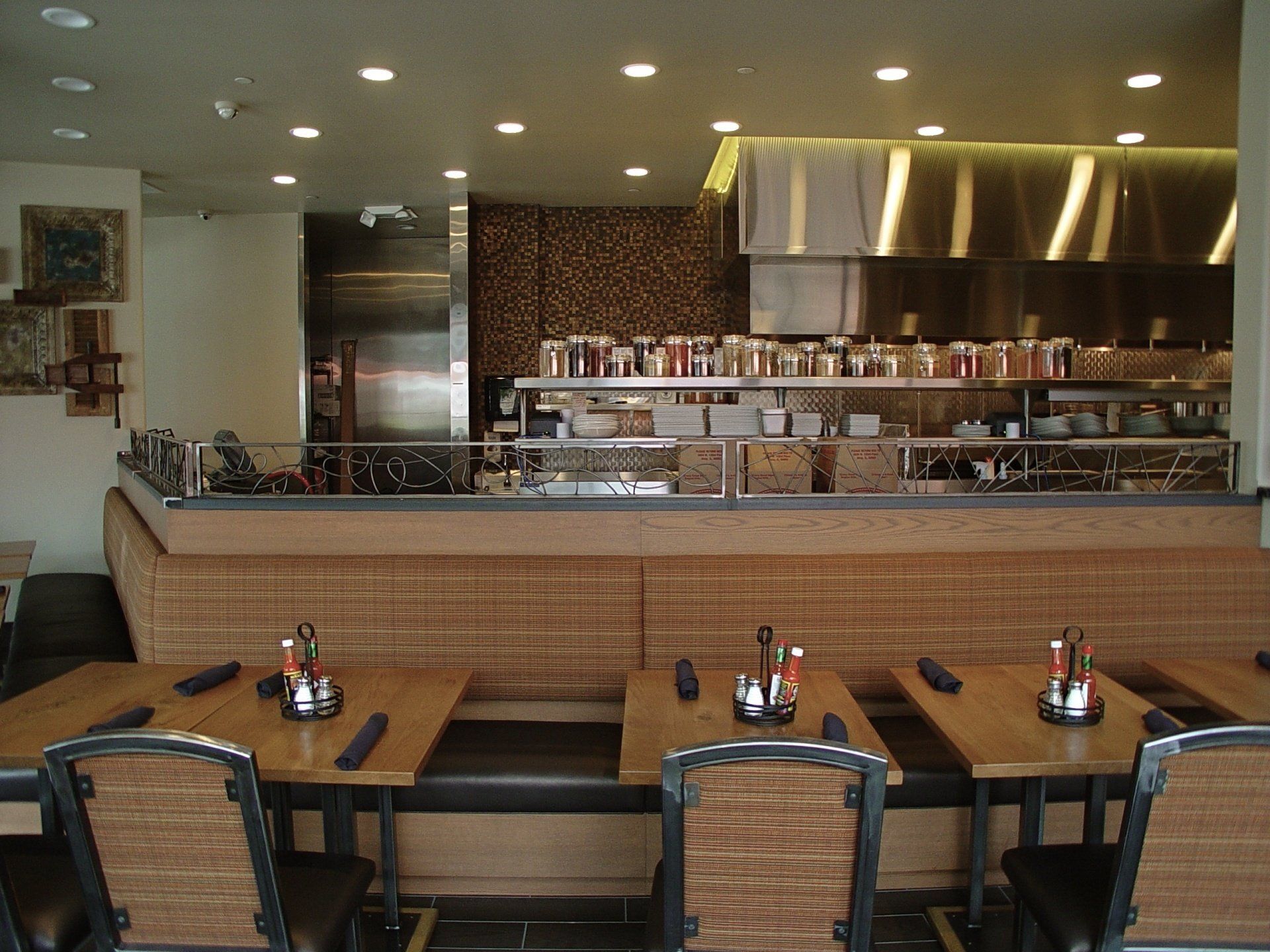 Restaurant interior with wooden booths and tables, open kitchen in background.