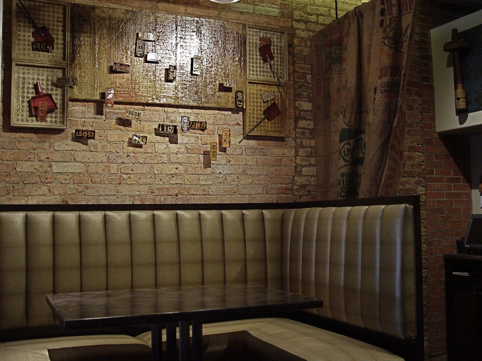 Booth seating in a dimly lit, rustic-style restaurant. Brick wall with artwork, dark table.