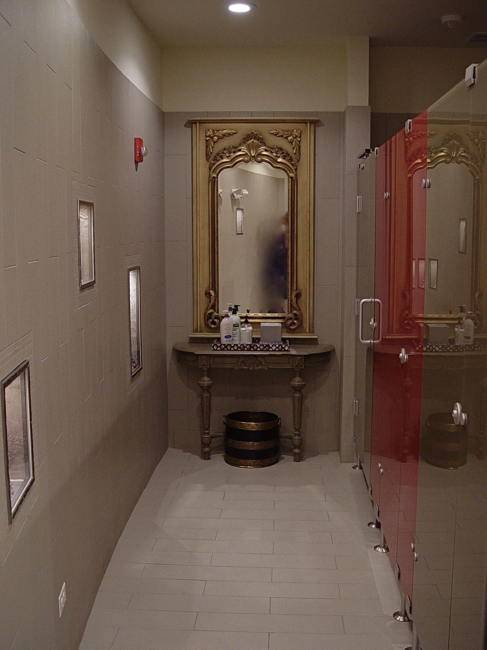 Narrow hallway with ornate mirror, decorative lights, and red-doored stalls.