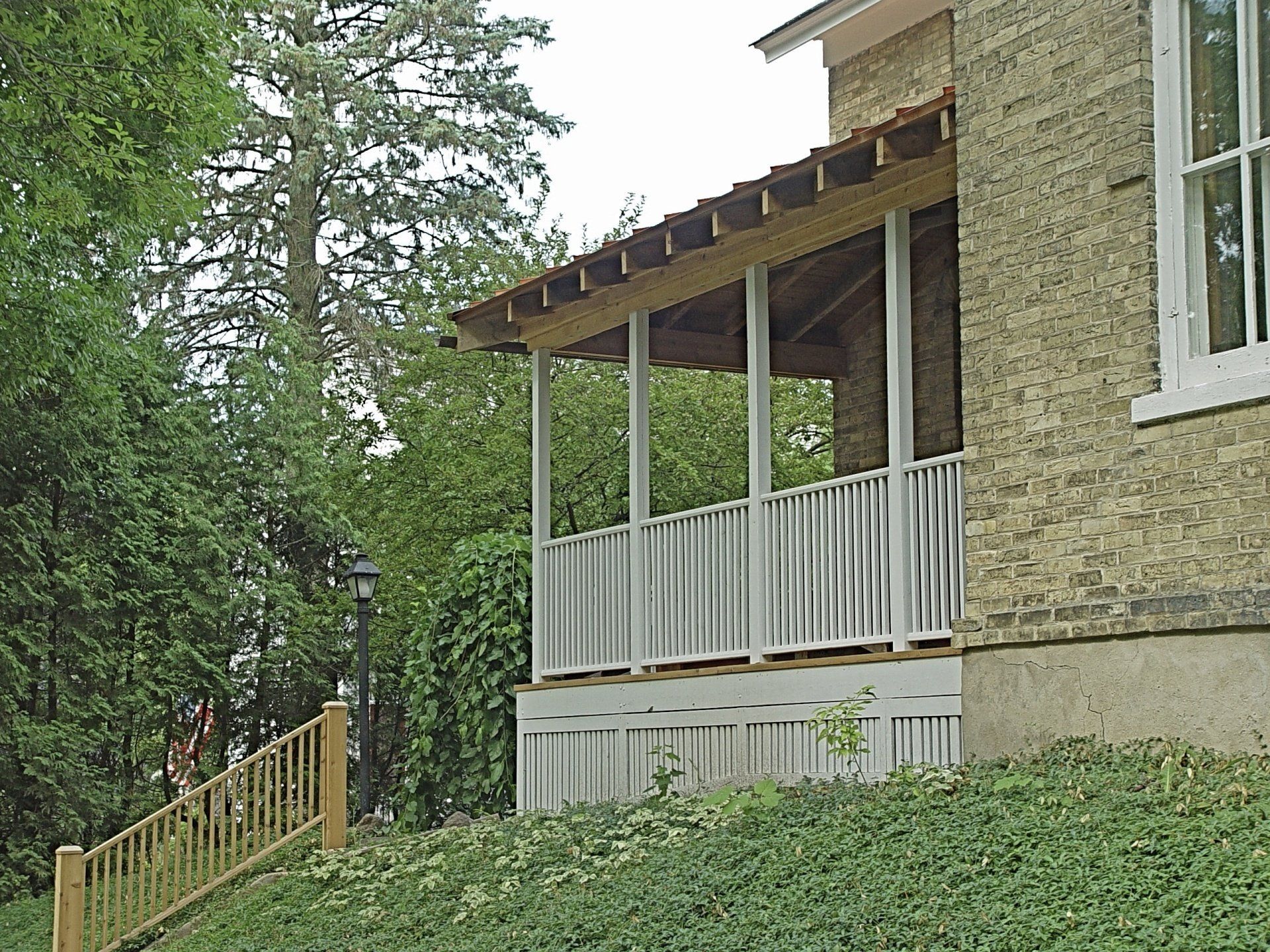Screened porch attached to a brick building; gray and white paint; railing, posts, and roof.