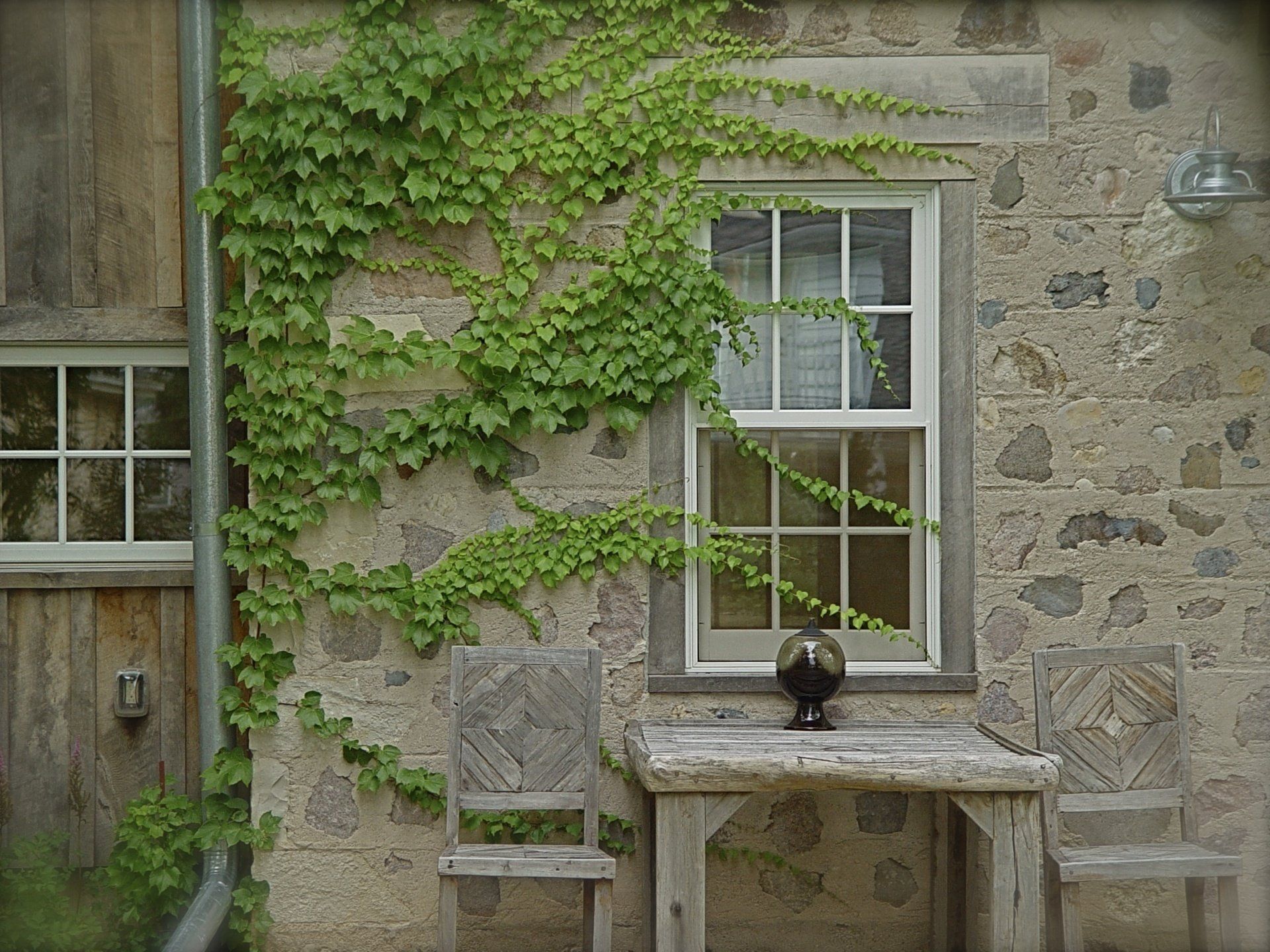 Stone building with a window and a wooden table and chairs, covered in ivy.