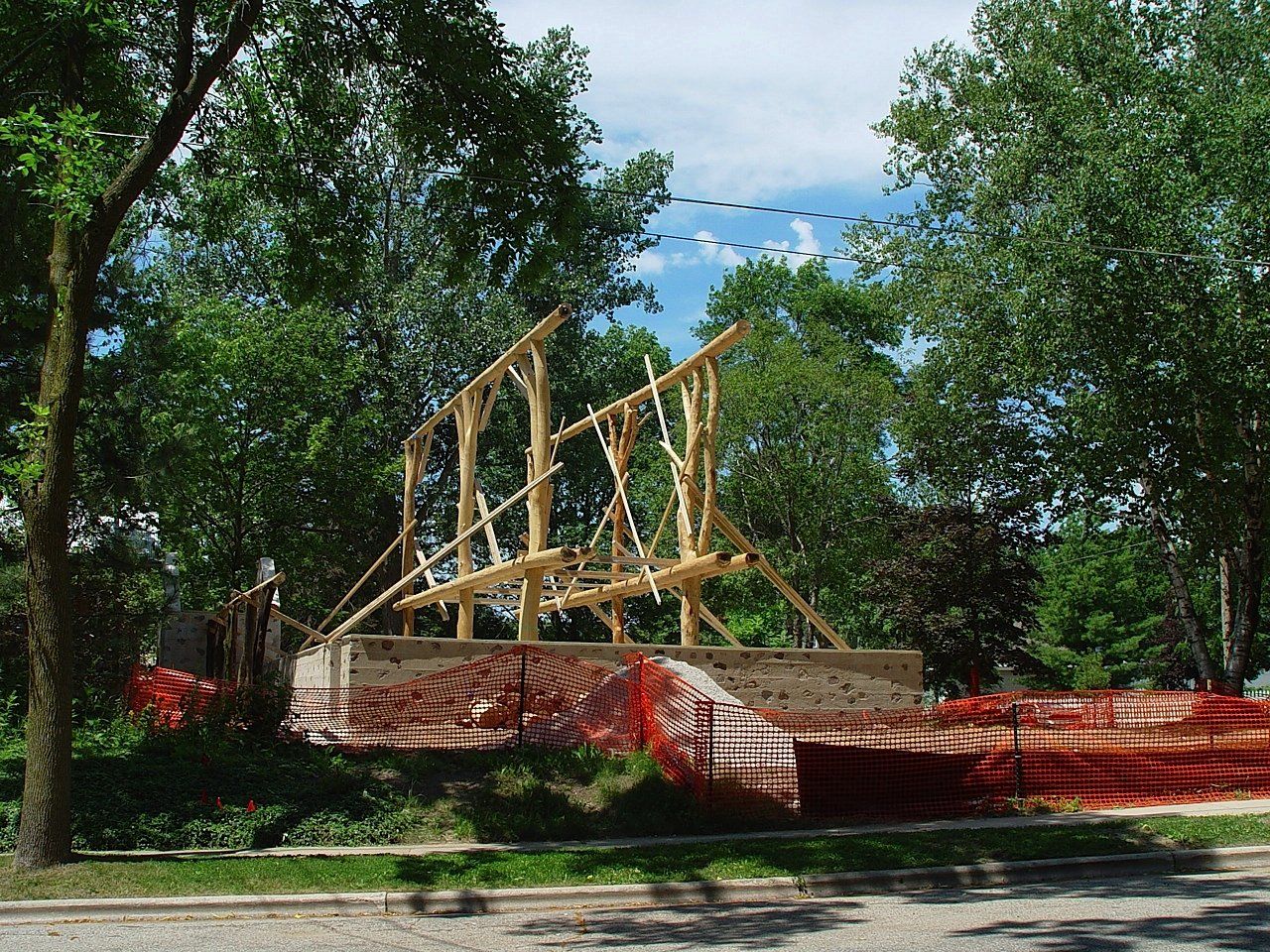Wooden frame construction on a foundation, surrounded by orange safety fencing and trees.
