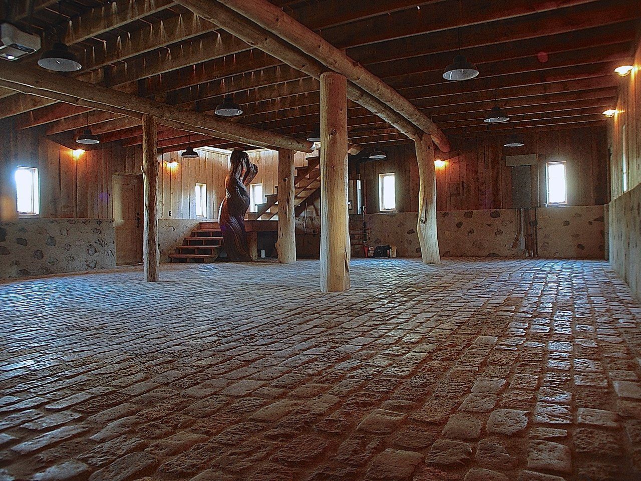 Rustic interior with cobblestone floor, wooden beams, and arched windows.