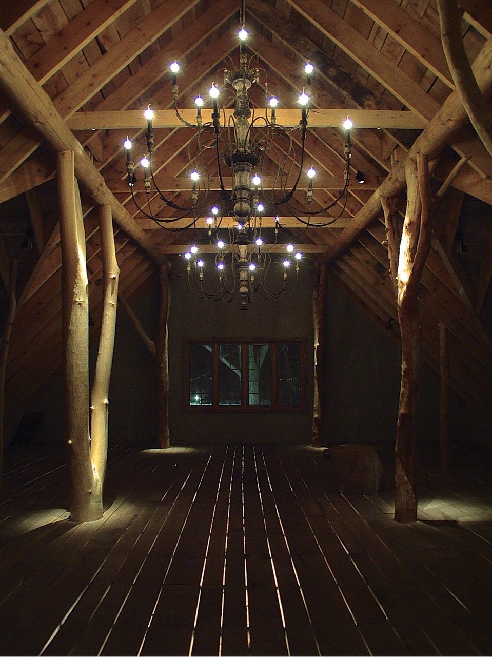 Wooden-beamed interior with chandelier and slatted floor. Dimly lit room with a window at the far end.