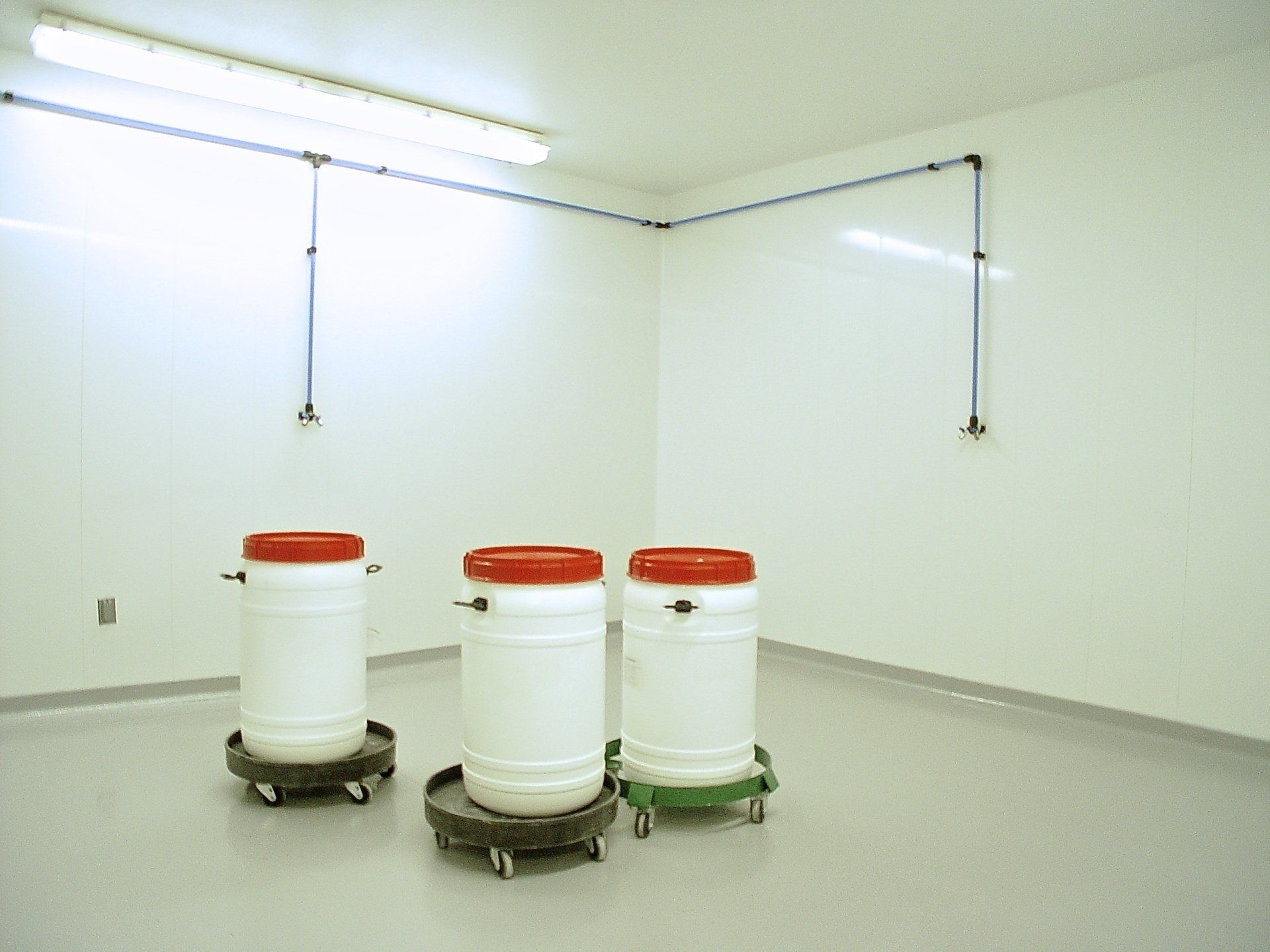 Three white barrels with red lids on rolling platforms in a sterile, white room.
