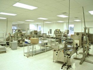 Factory interior with machinery, stainless steel tables, and bright fluorescent lights.