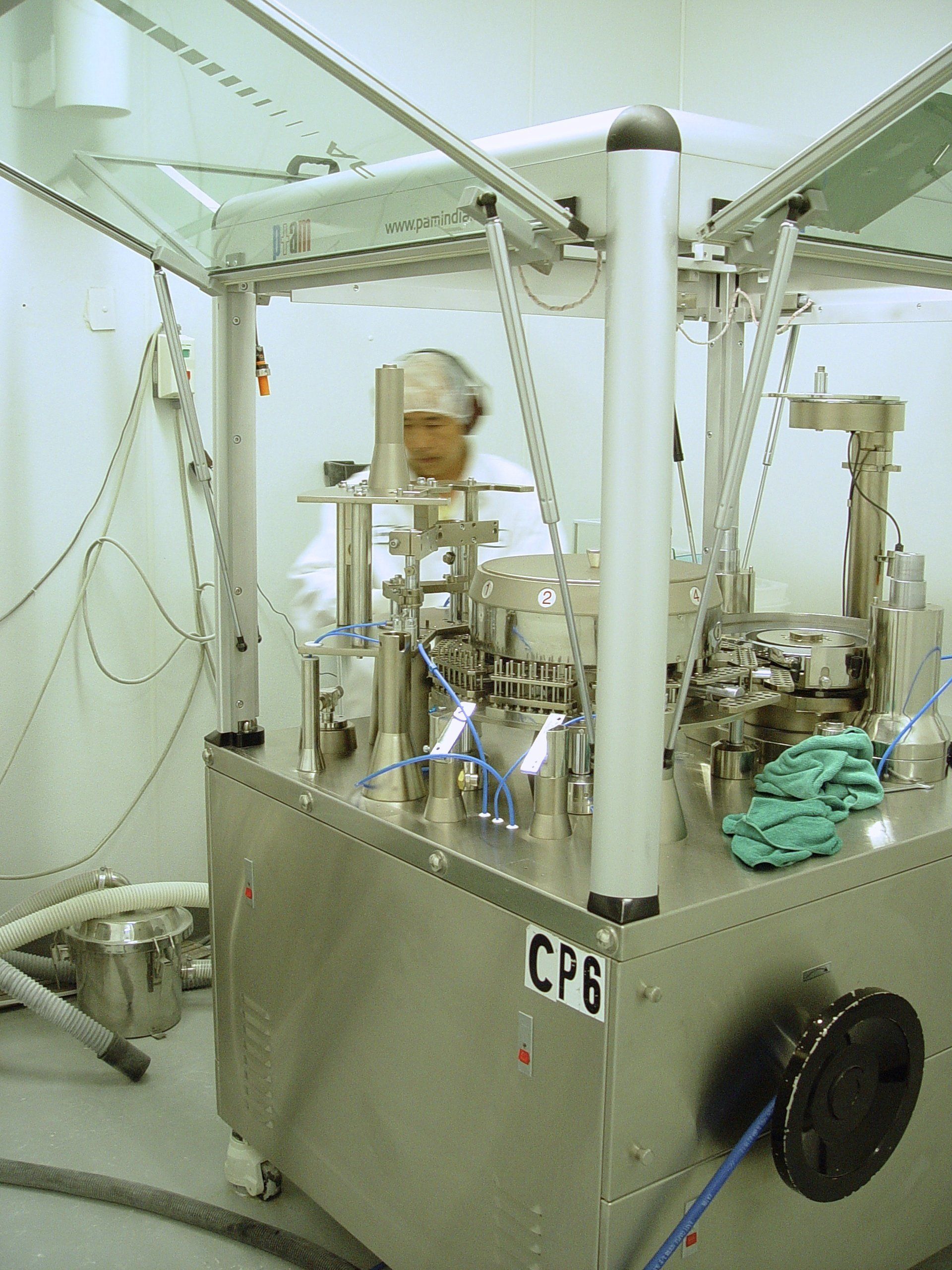 A person in a lab coat operates machinery inside a stainless steel enclosure.