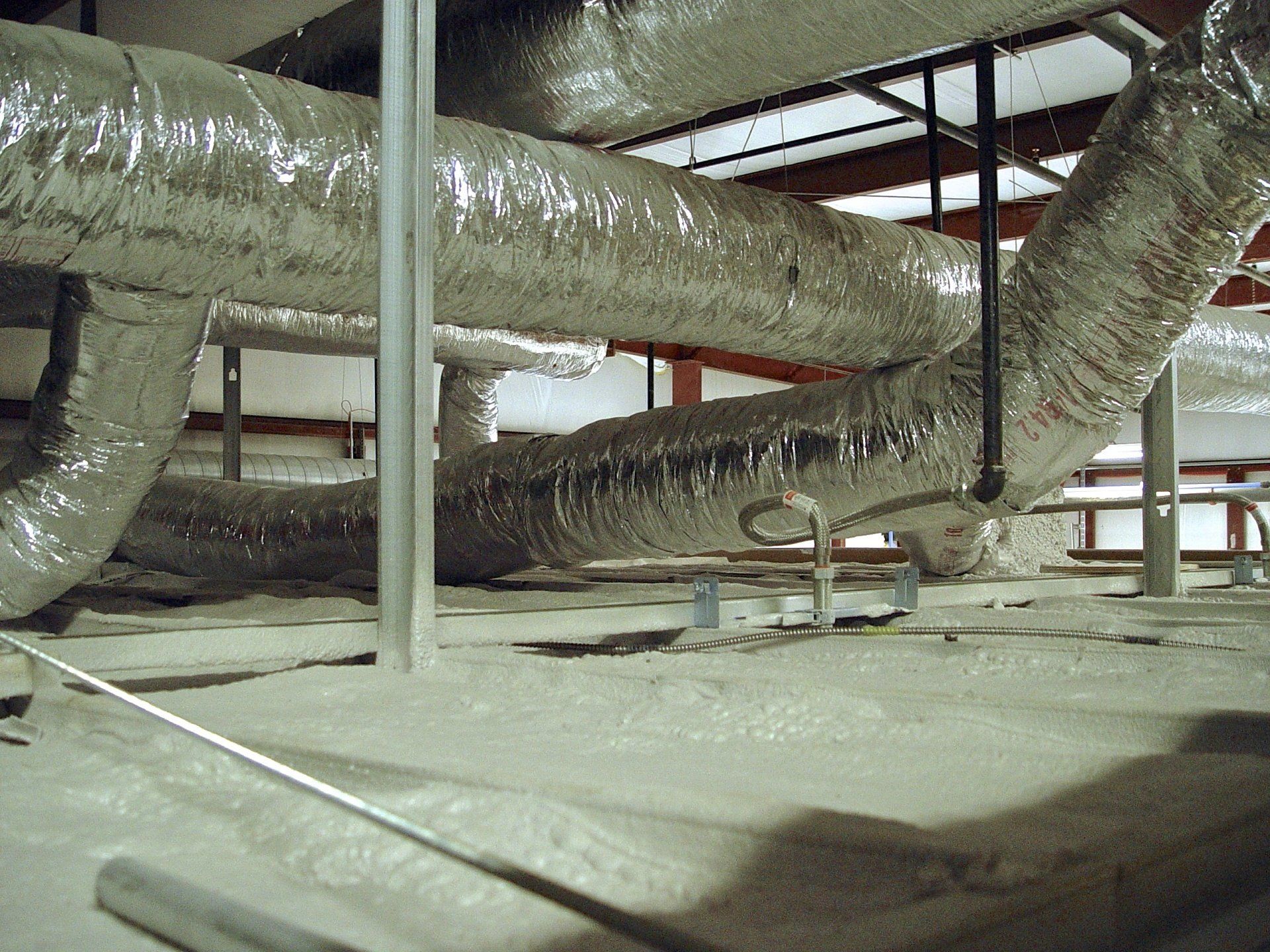 HVAC ductwork in a building. Insulated, metallic tubes run across the ceiling.
