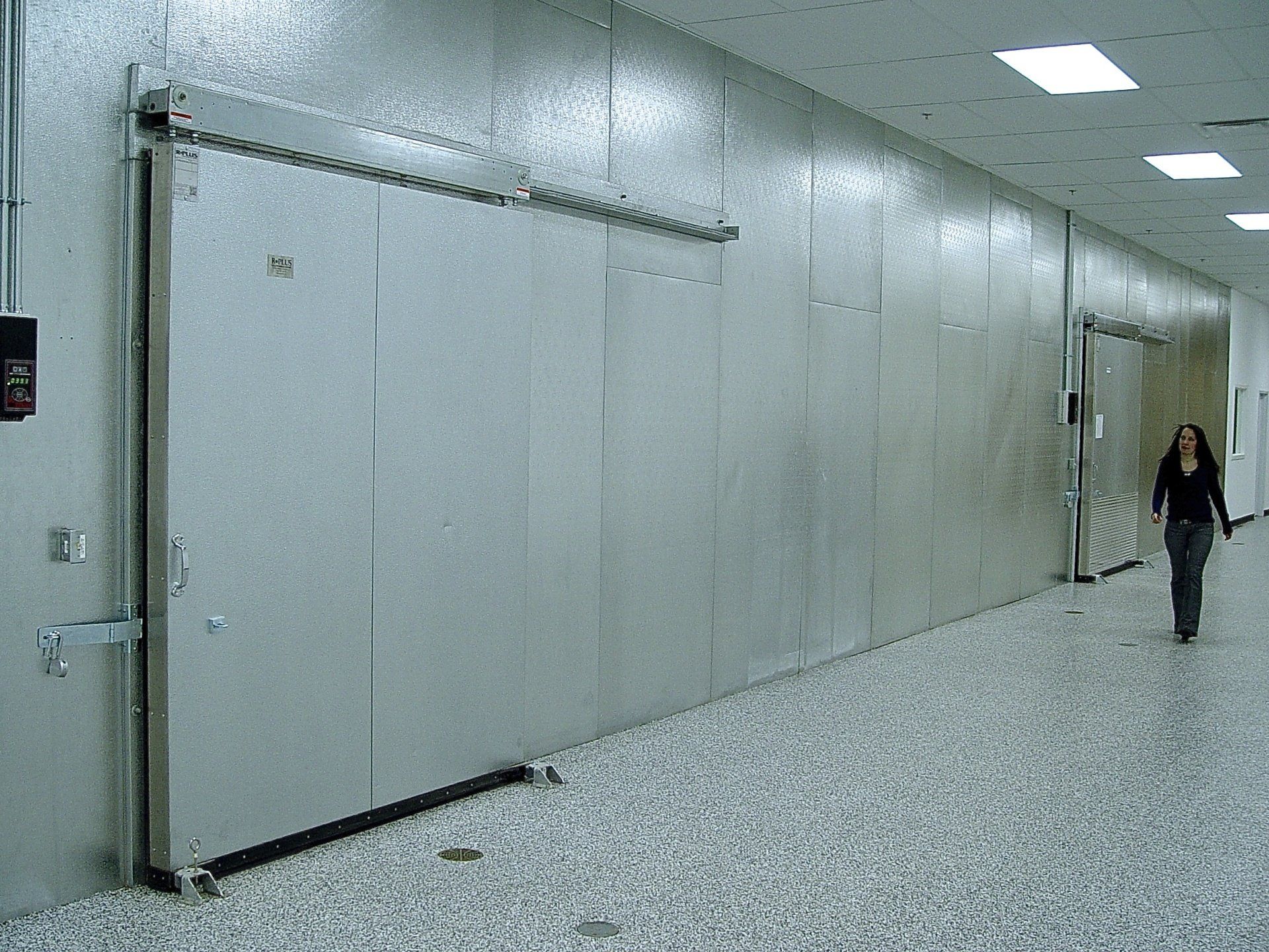 Hallway with large metal doors, a person walking towards a door.