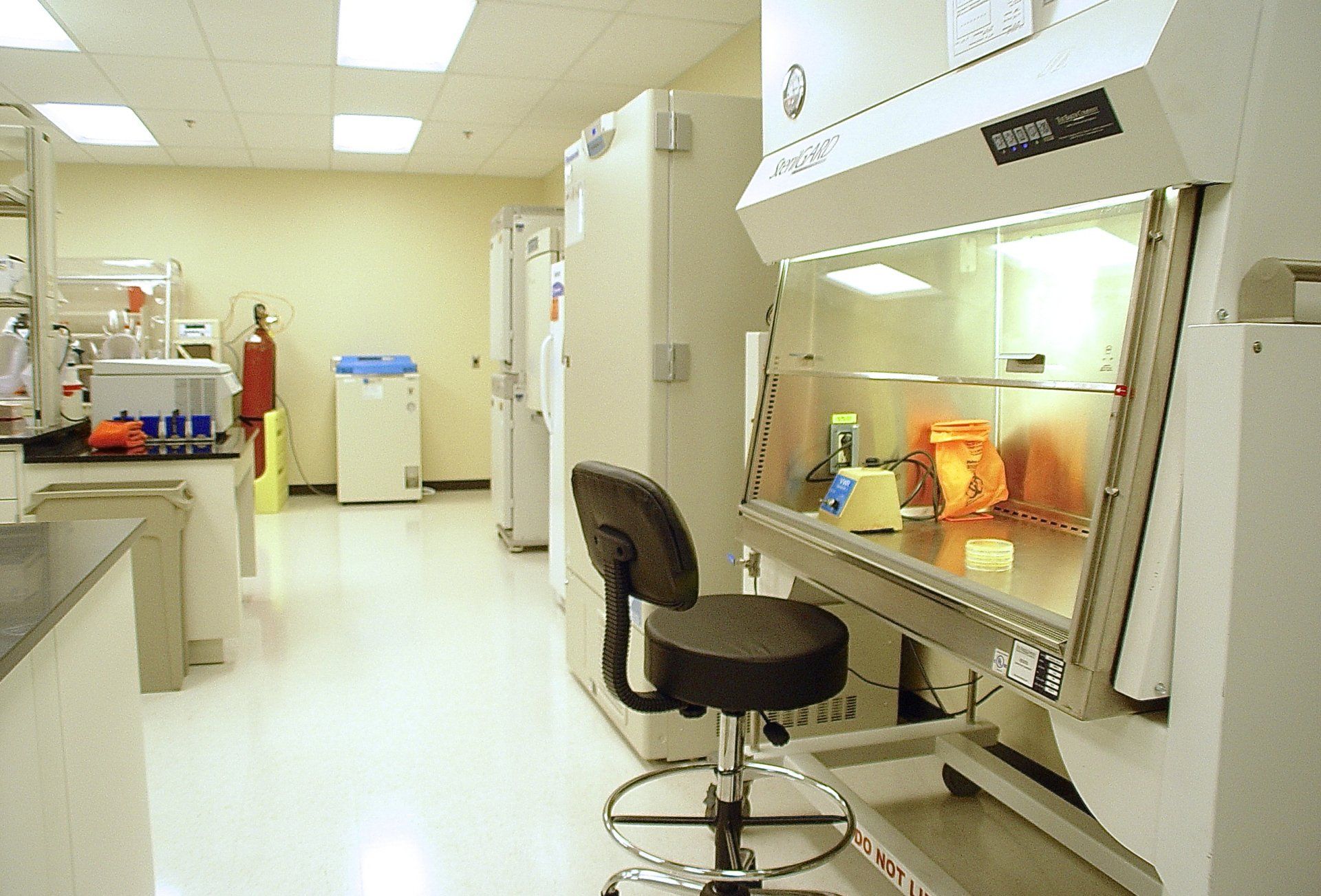 Laboratory with equipment, including a fume hood and lab benches. An office chair is in front of the hood.
