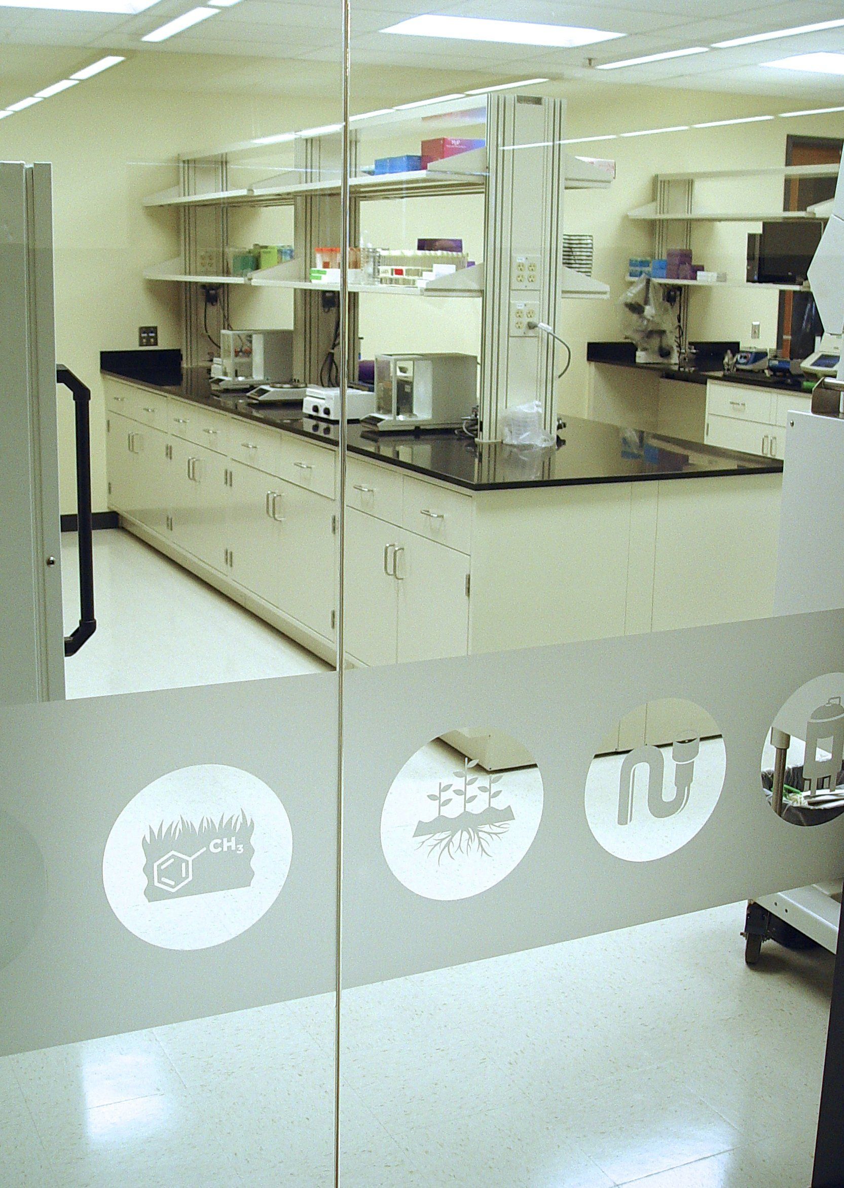 Laboratory interior with lab benches, equipment, and frosted glass door with symbols.