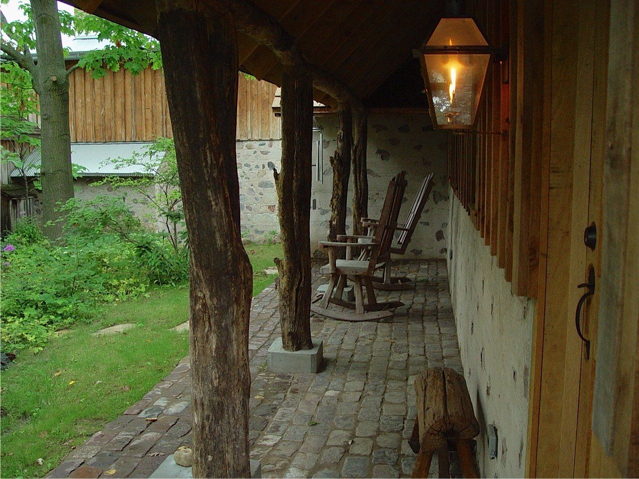 Covered porch with rustic wood posts, brick path, rocking chairs, and lit lantern.
