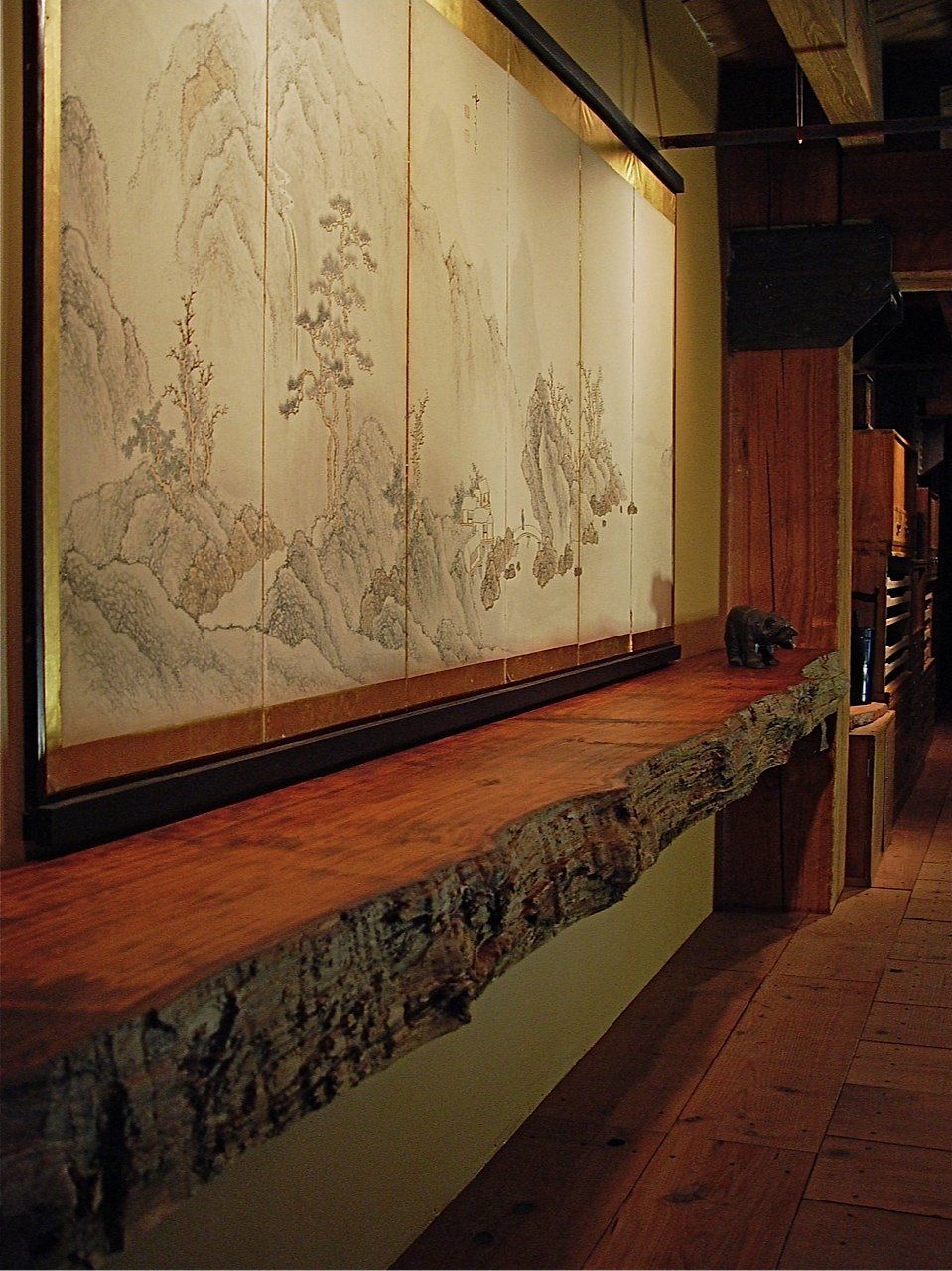 Rustic wooden shelf beneath a traditional landscape painting. Interior with wooden beams and floor.