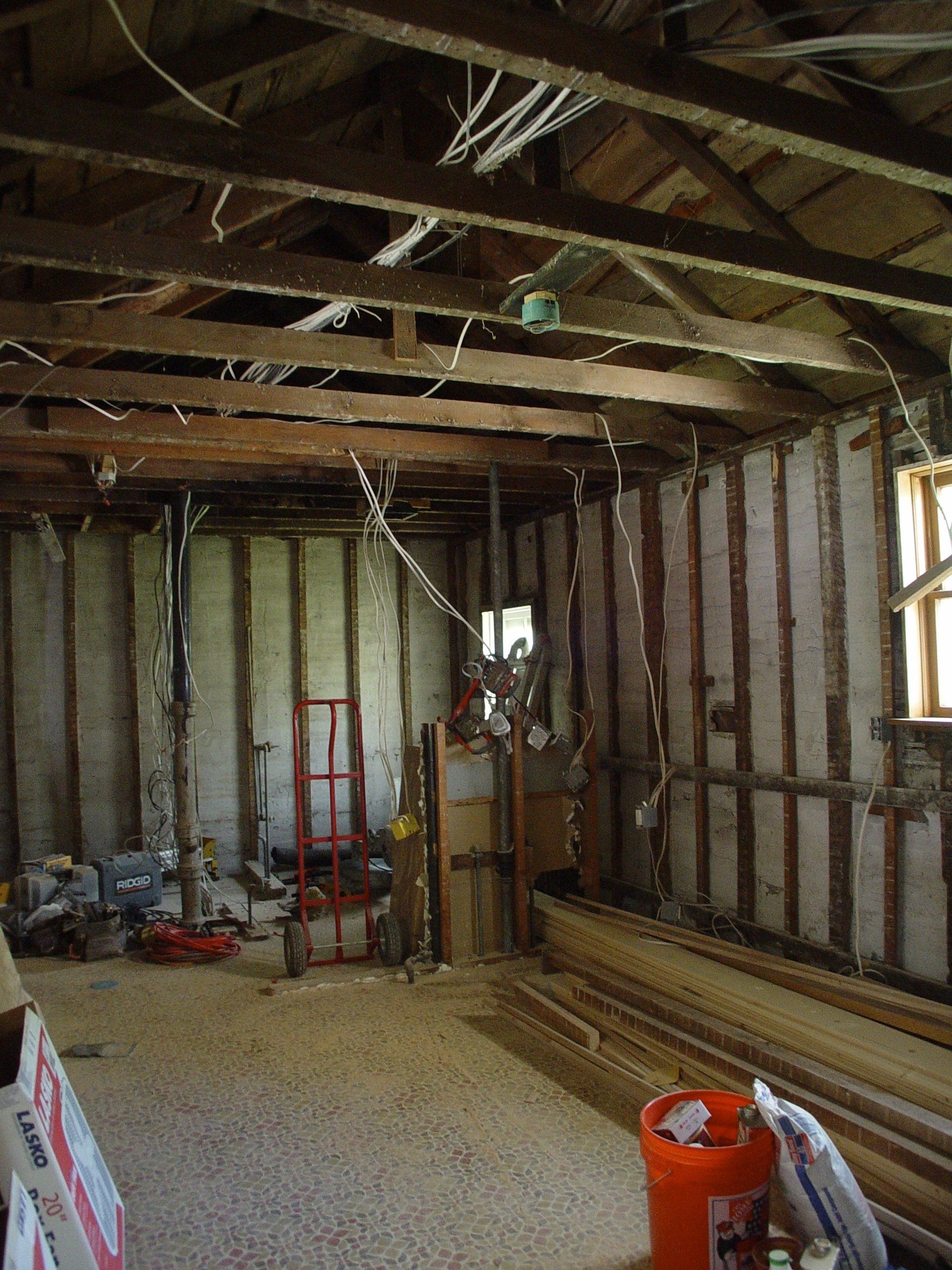 Interior of a dilapidated room under renovation; exposed wooden beams, studs, and wiring; debris on floor.