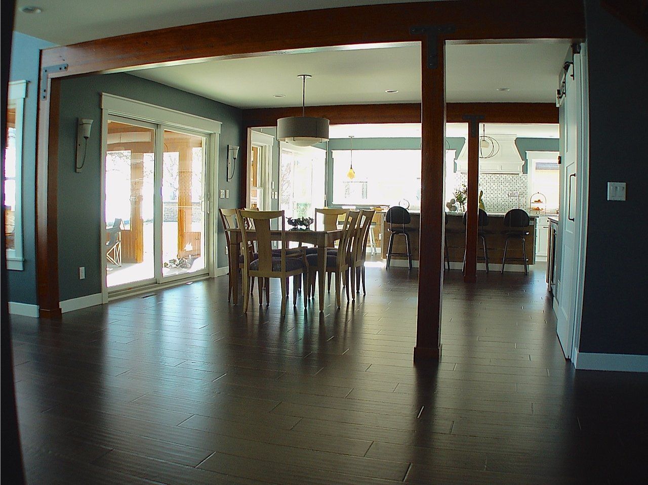 Spacious dining room with dark wood floors, a round table, and a view of a deck through glass doors.