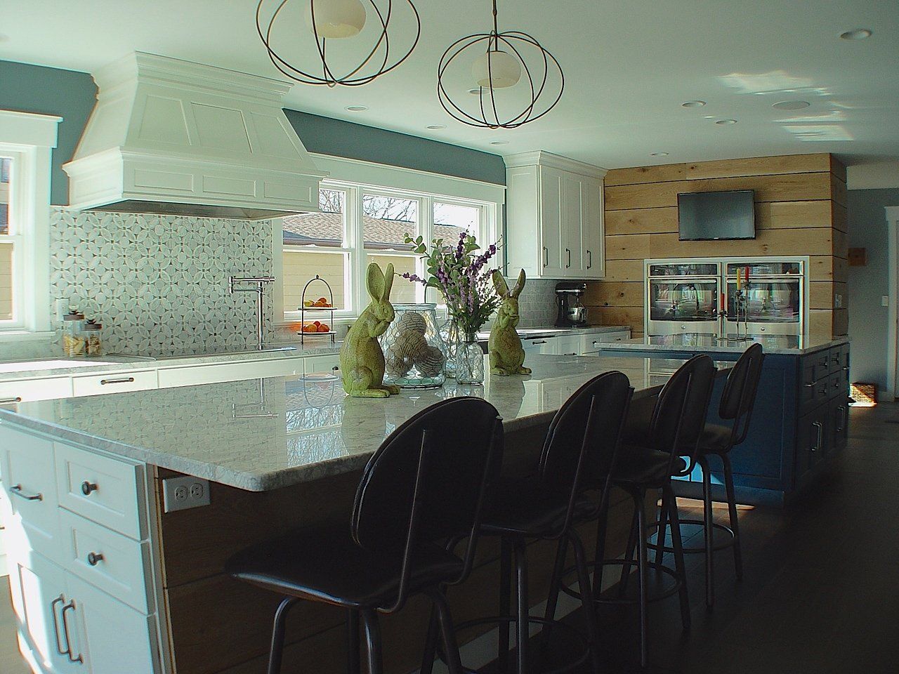Spacious kitchen with large island, granite countertop, stools, and white cabinets. Blue accent wall, decorative lighting.