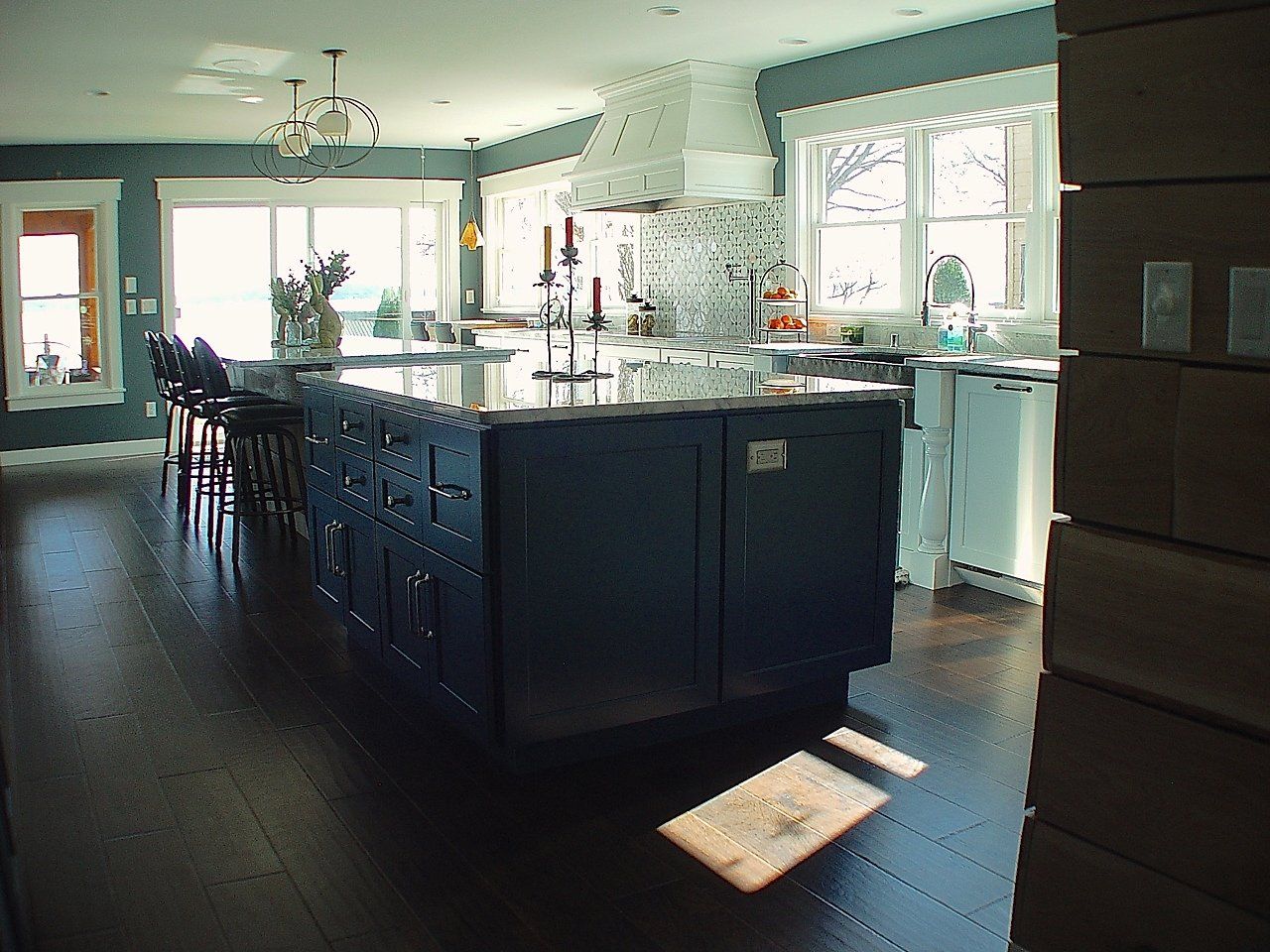 Dark blue kitchen island with a dark wood floor and a large white range hood.