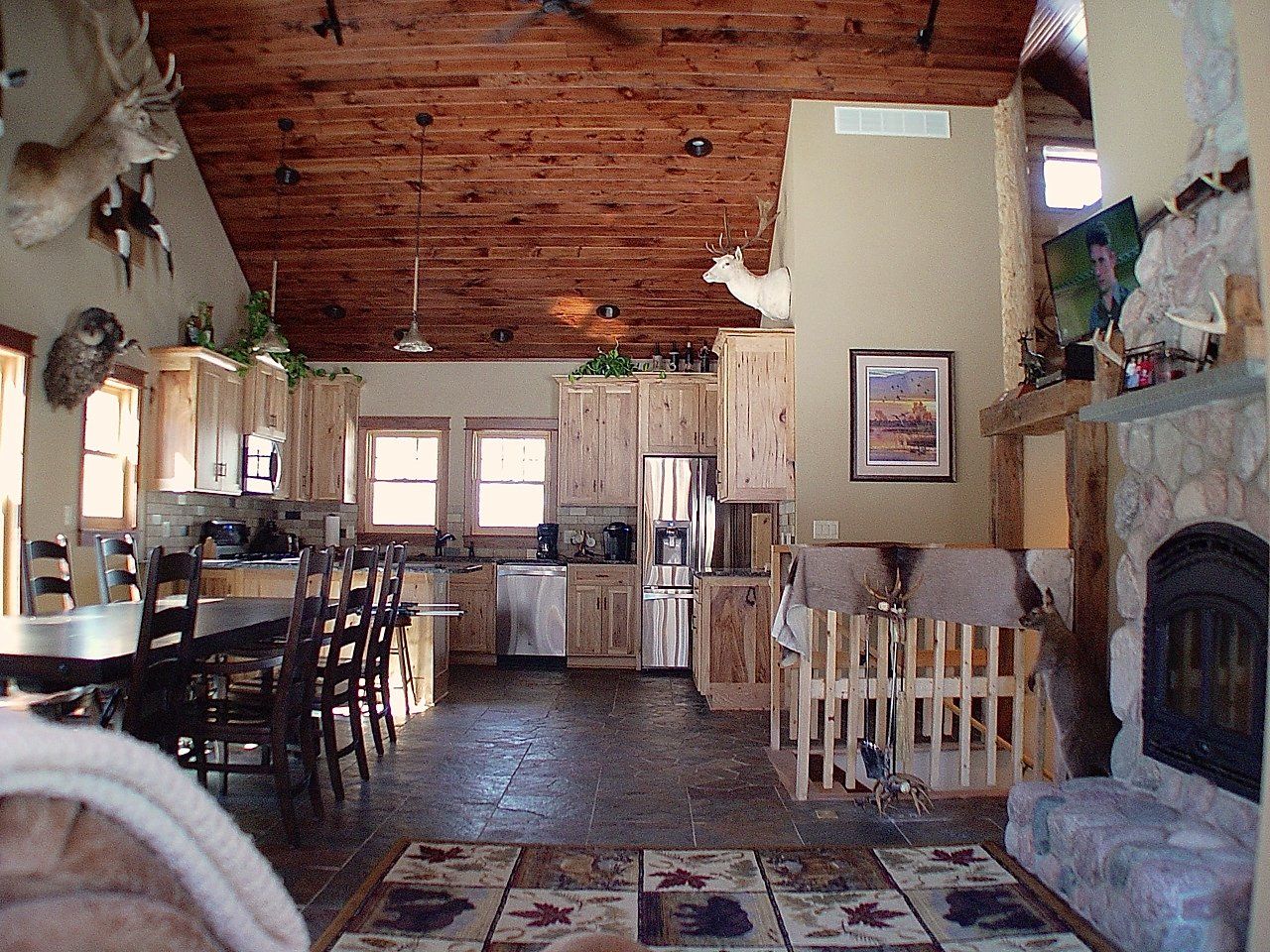 Rustic kitchen and living area with wood ceiling, cabinets, fireplace, and taxidermy.