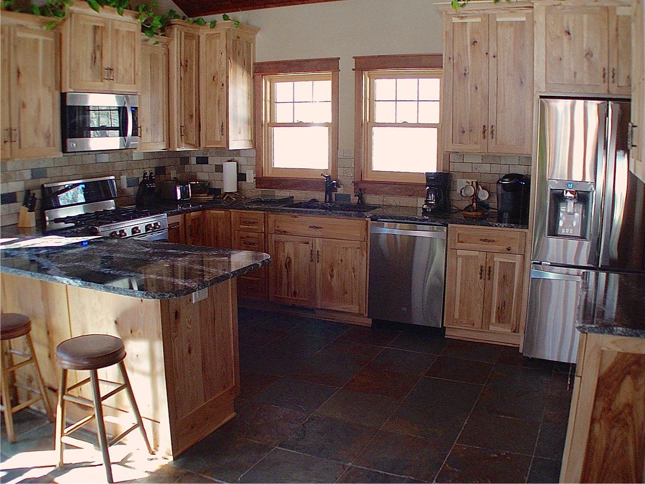 Kitchen with light wood cabinets, granite countertops, stainless steel appliances, and a dark tile floor.
