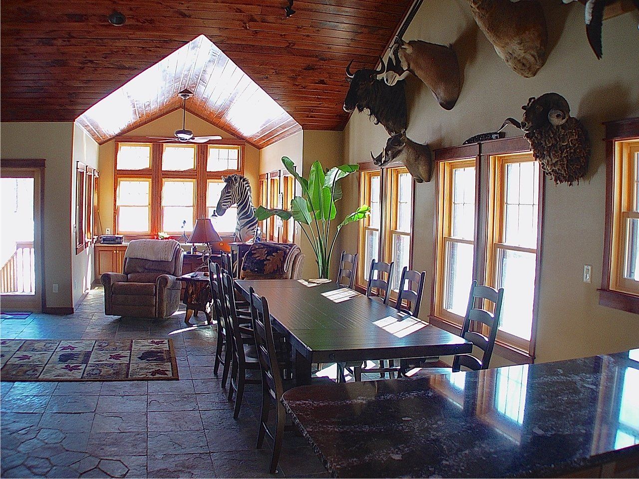 Large room with dining table, seating area, taxidermied animal heads on wall, wood ceiling and windows.