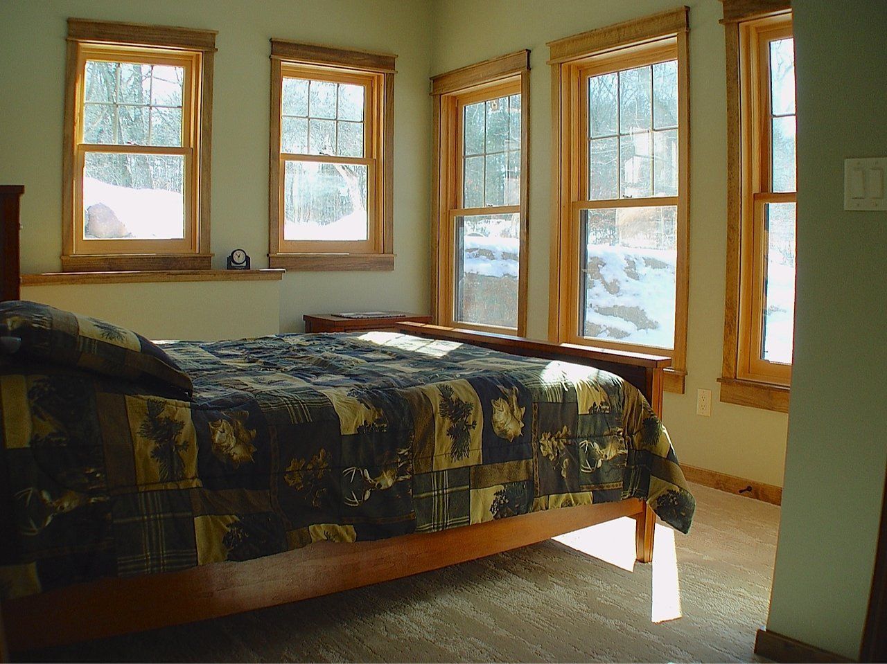 Bedroom with wooden-framed windows, bed with patterned cover, light green walls, and beige carpet.