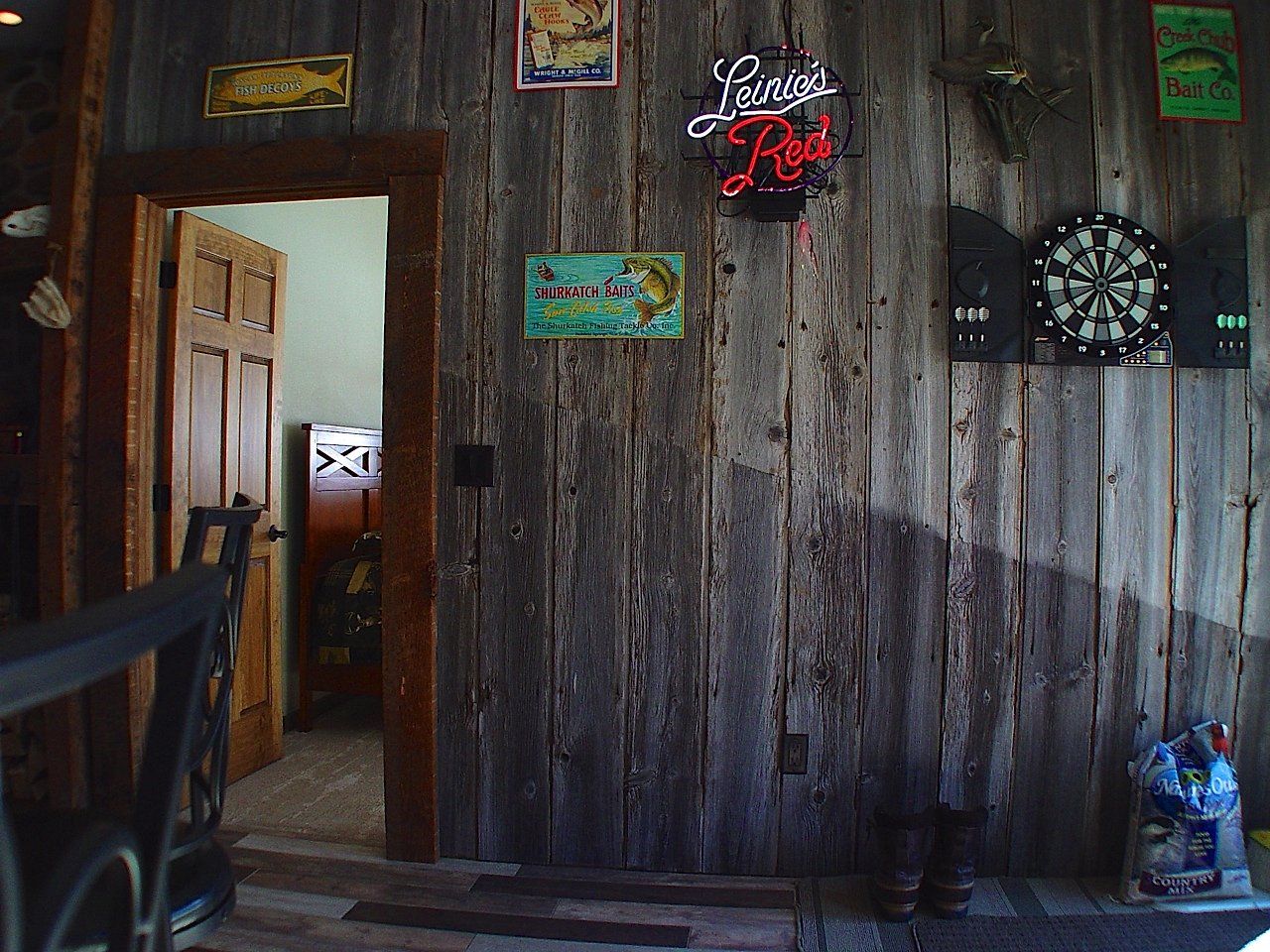 Rustic interior with wooden walls, a door, dartboard, and neon sign.