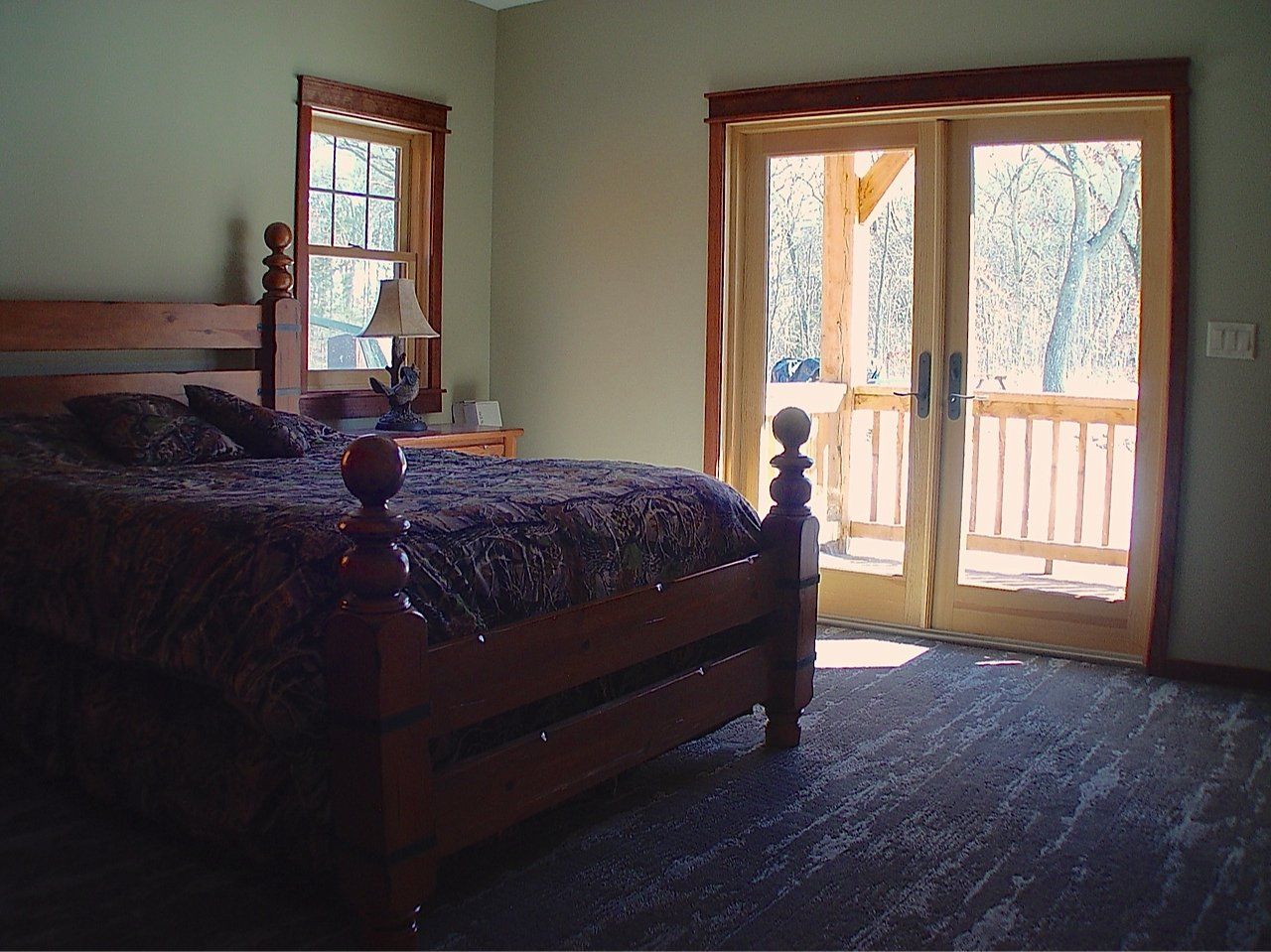 Bedroom with wooden bed, nightstand, and double doors leading to a porch with sunlight.