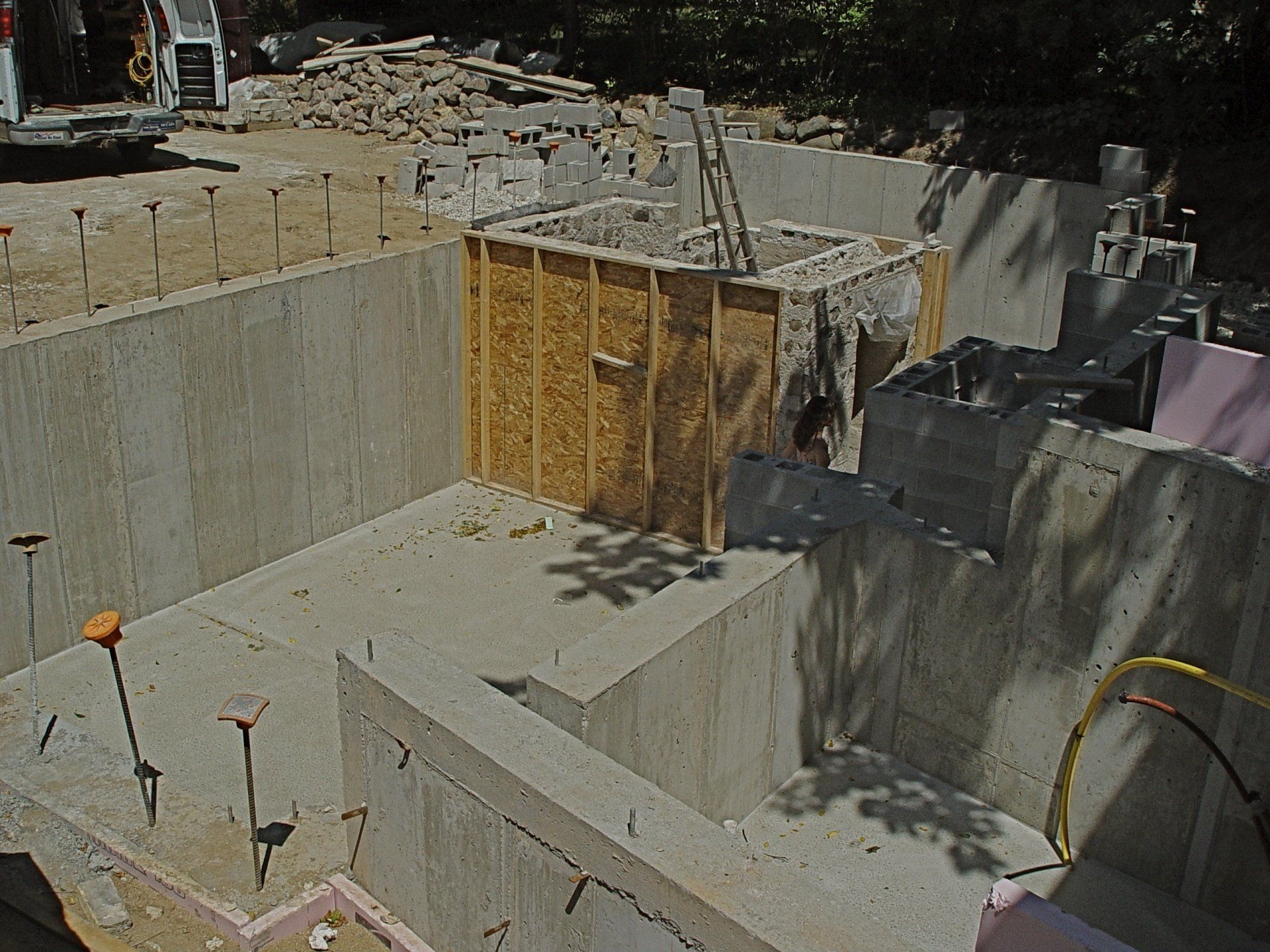 Construction site, concrete foundation with wooden forms, mini-excavator in background.
