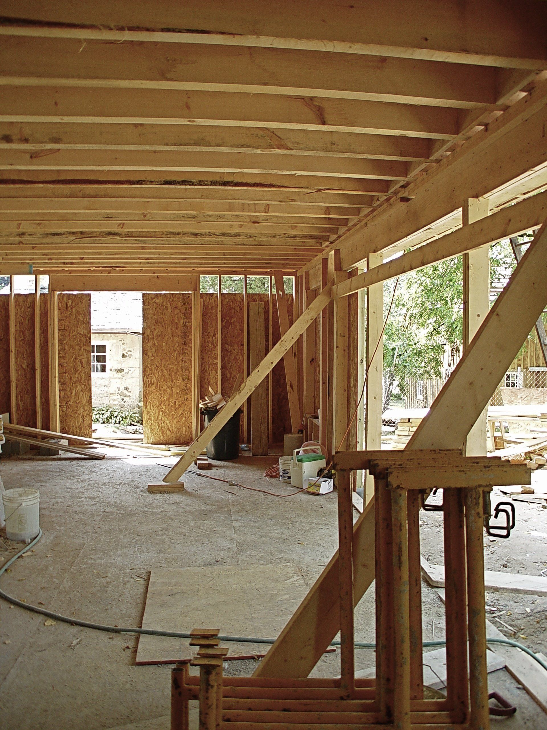 Interior view of a building under construction, showing wooden framing, beams, and open walls.