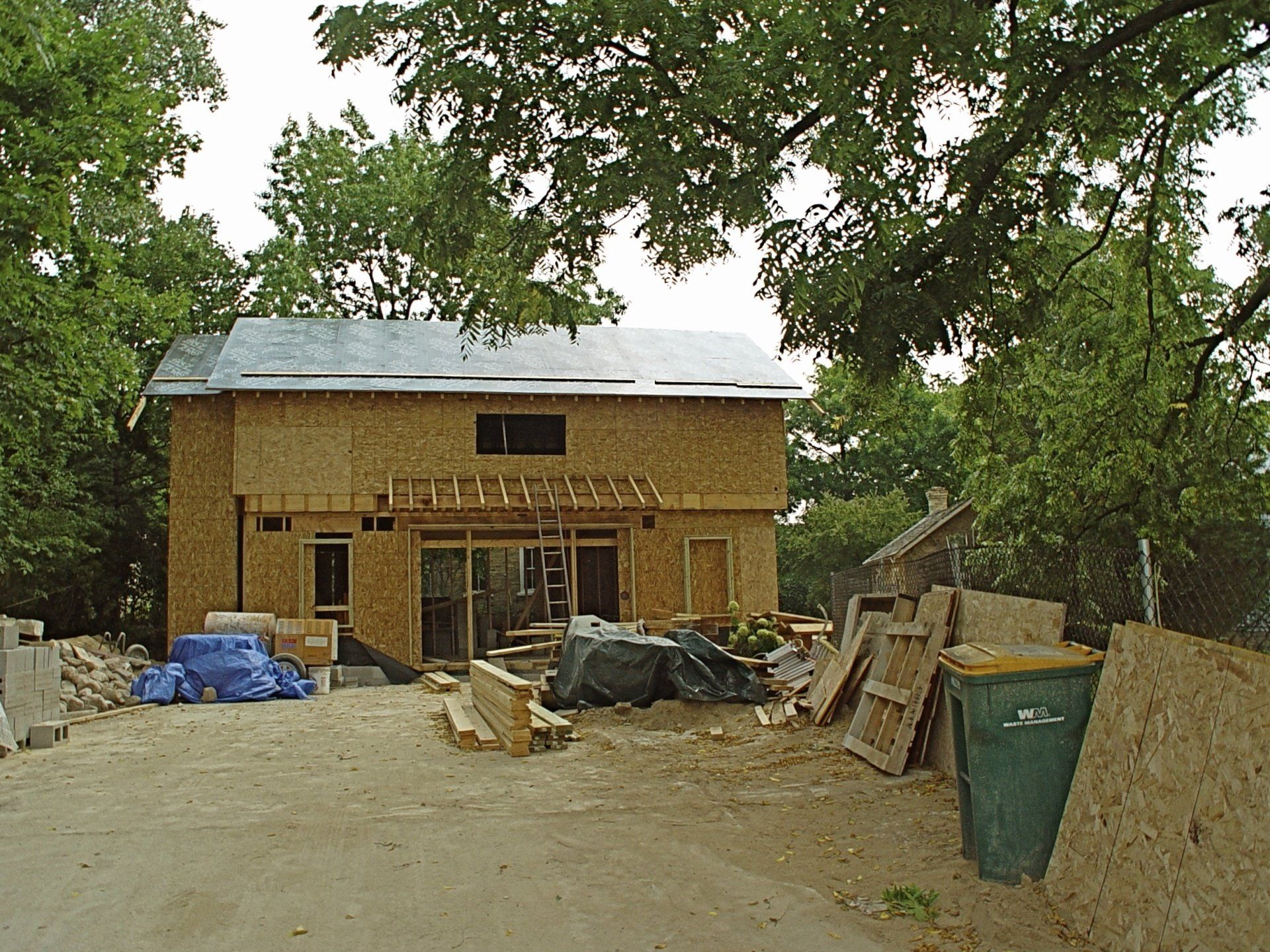 Two-story house under construction, surrounded by trees and construction materials in a yard.