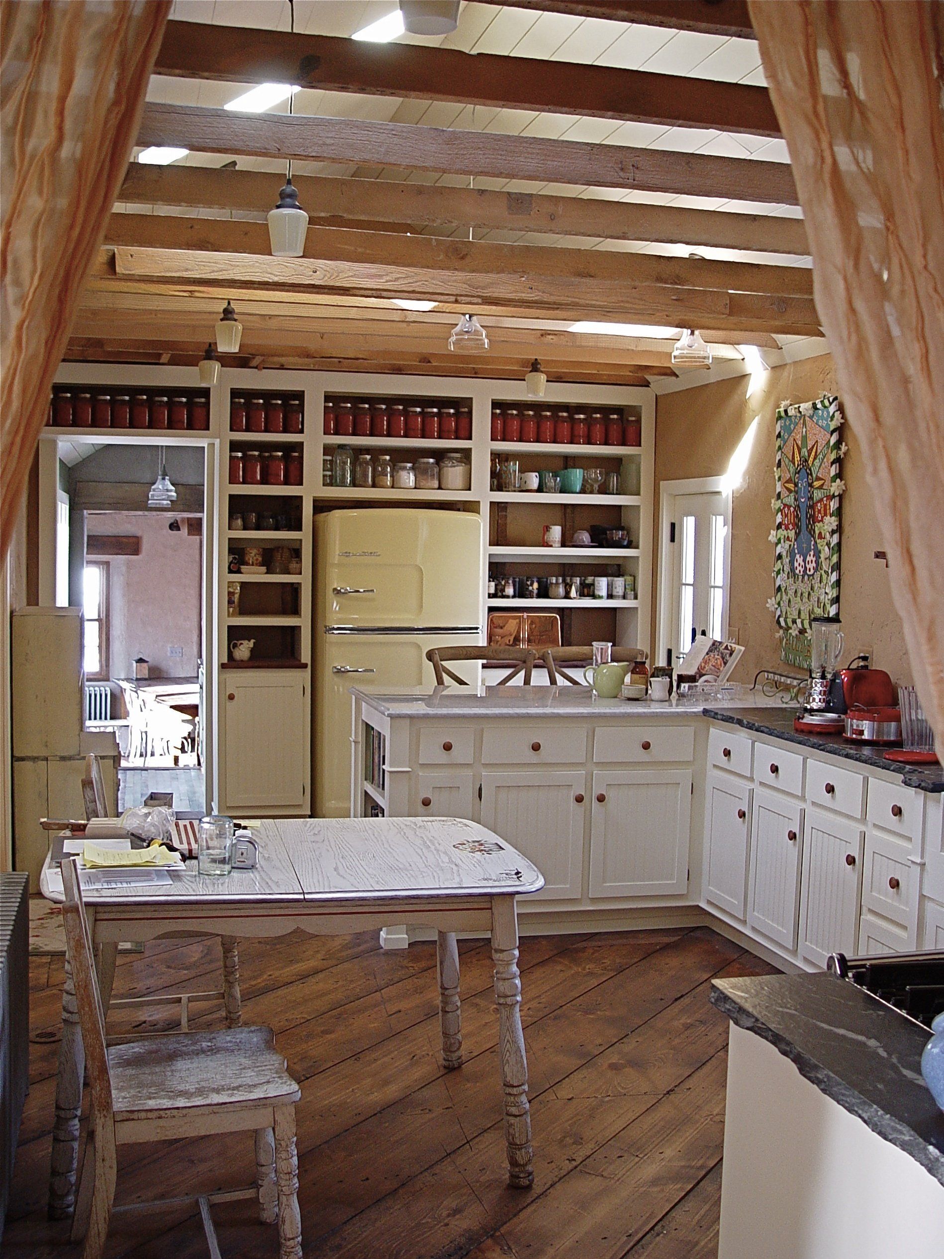 Rustic kitchen with wood beams, white cabinets, yellow refrigerator, and jars on shelves.