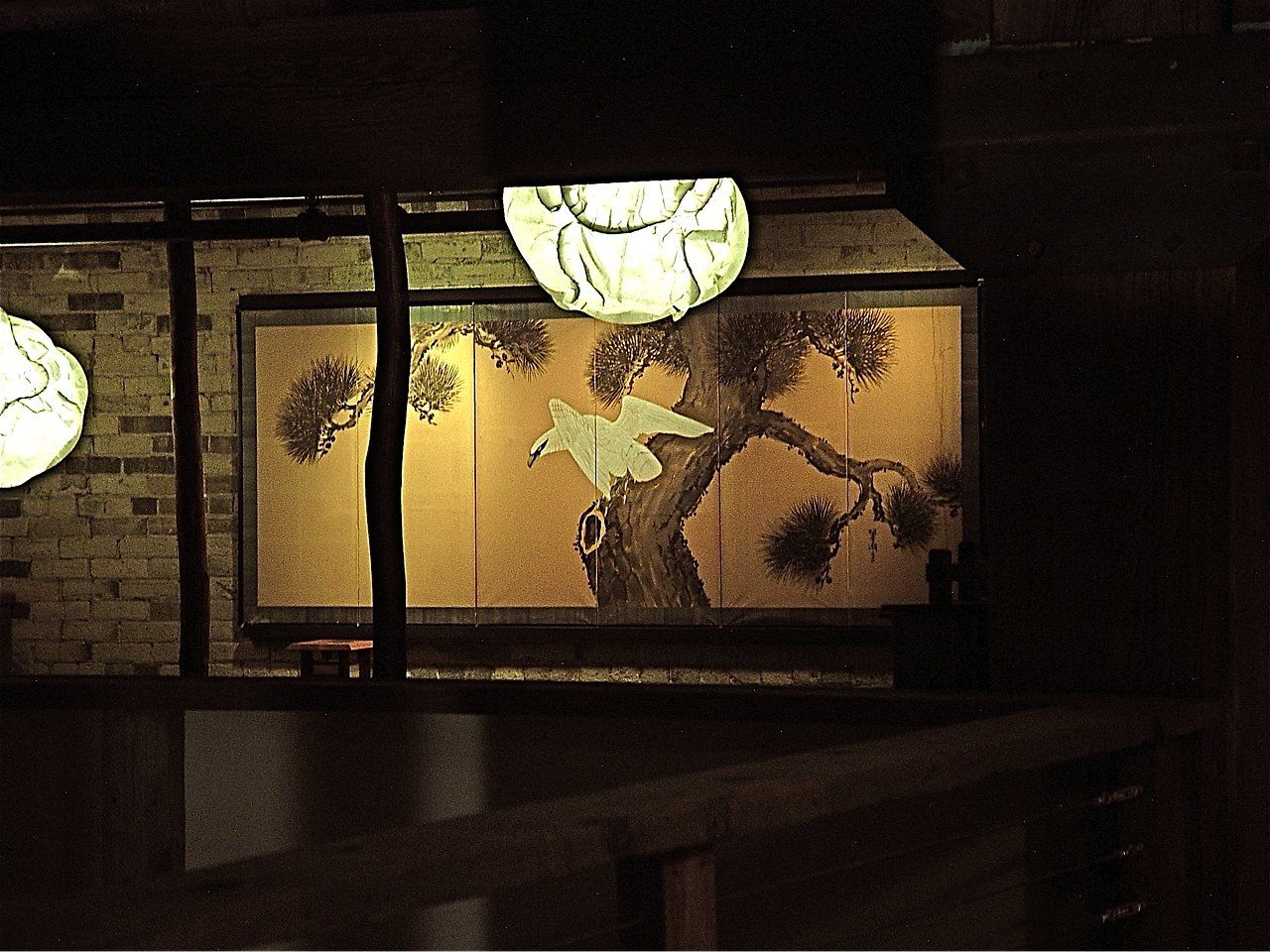 Lit lantern illuminates an Asian-style painting with a tree and a bird, set in a dimly lit space.