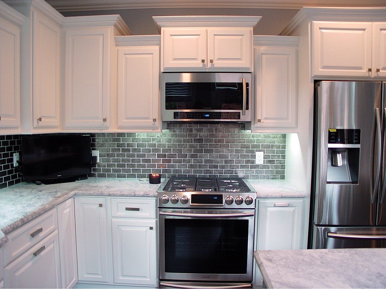 White kitchen with stainless steel appliances, mosaic backsplash, and granite countertops.