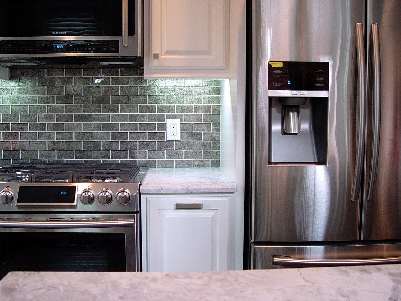 Kitchen interior with stainless steel appliances, white cabinets, and gray tiled backsplash.