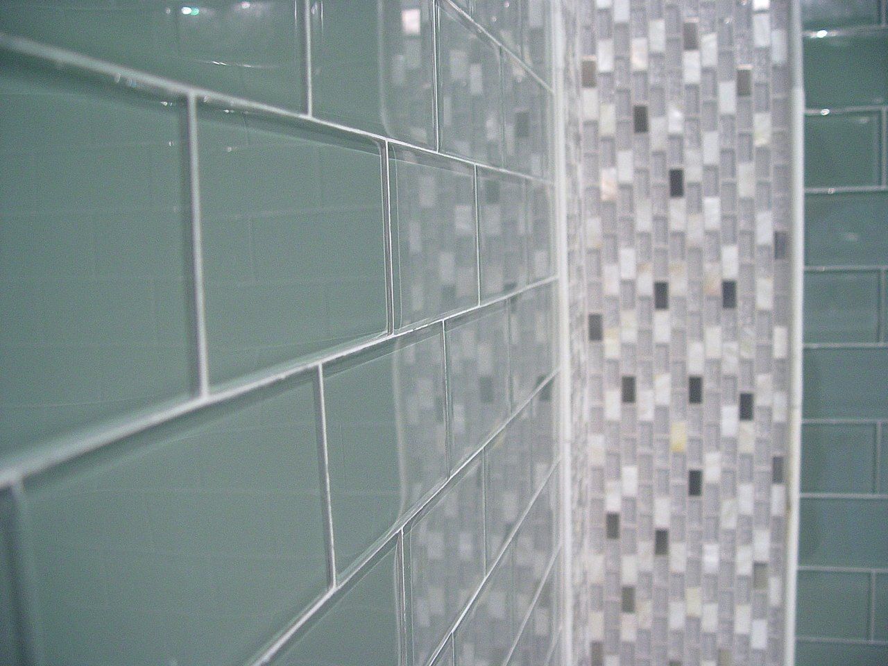 Green rectangular tiles with white grout meet a mosaic border in a bathroom.
