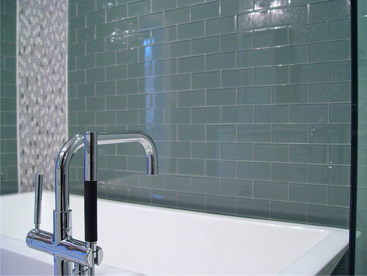 Modern bathroom with a white bathtub and chrome faucet against teal subway tile.